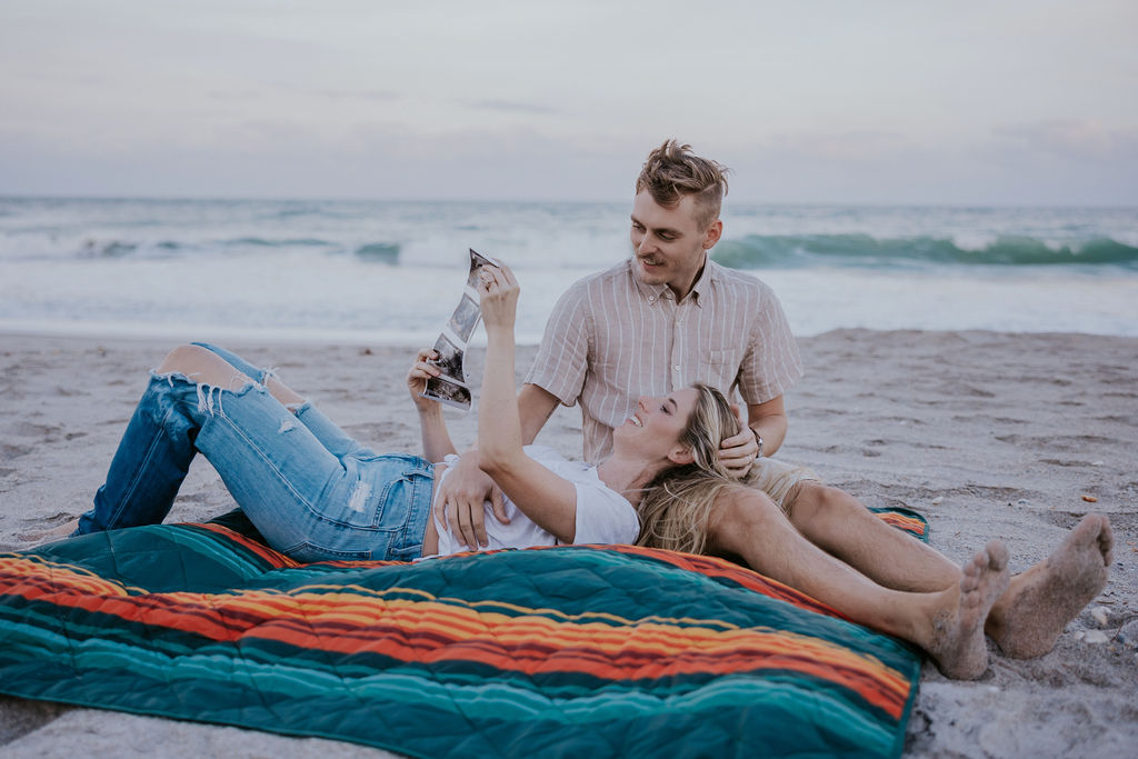 Destination Wedding Photographer captures couple sitting on blanket together looking at ultrasound pictures 