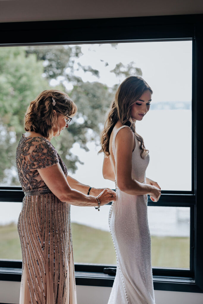 Destination wedding photographer captures mother helping bride into wedding dress before romantic Minnesota wedding