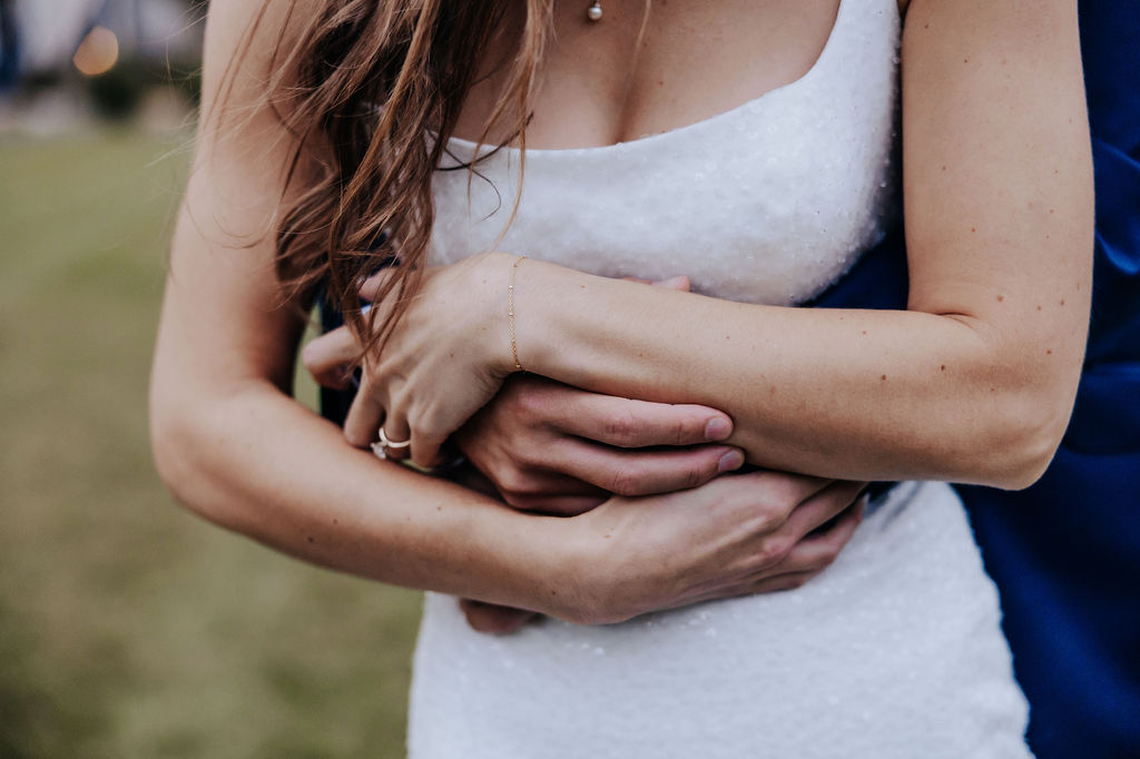 Close-up of the bride and groom’s arms wrapped tightly around each other, showing connection and love on their wedding day.
