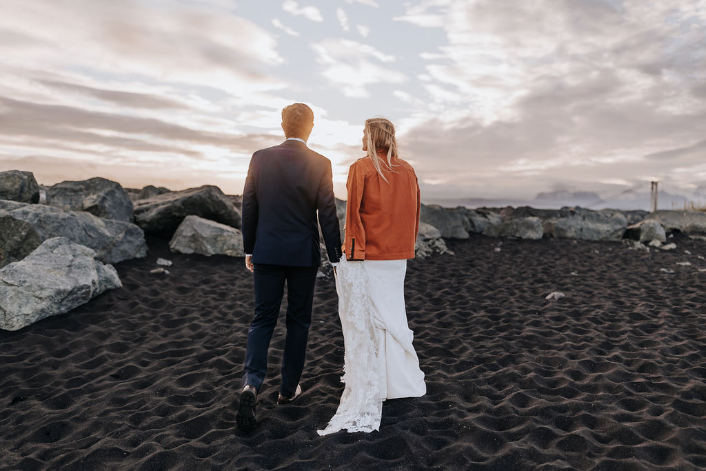 Destination wedding photographer captures bride and groom walking on black sand beach in Iceland after they chose to elope in Iceland