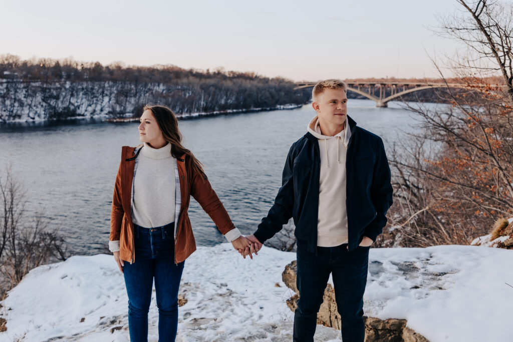 Destination Wedding Photographer captures man and woman holding hands in snow during winter engagement photos