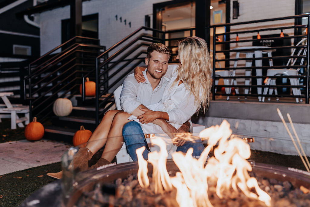 Nashville Engagement Photographer captures woman sitting on man's lap in front of fire before making smores