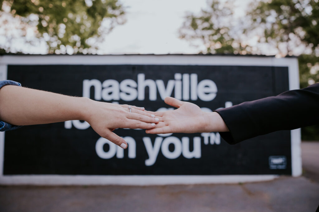 Destination Wedding Photographer captures couple holding hands in front of Nashville sign