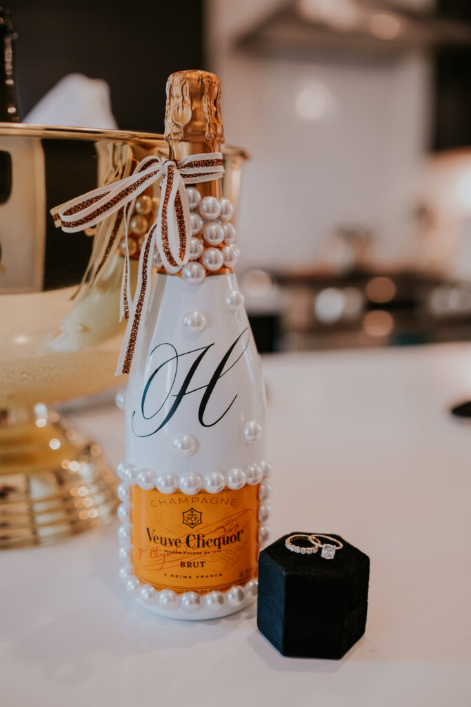 Bedazzled champagne bottle sitting on counter with wedding rings next to it