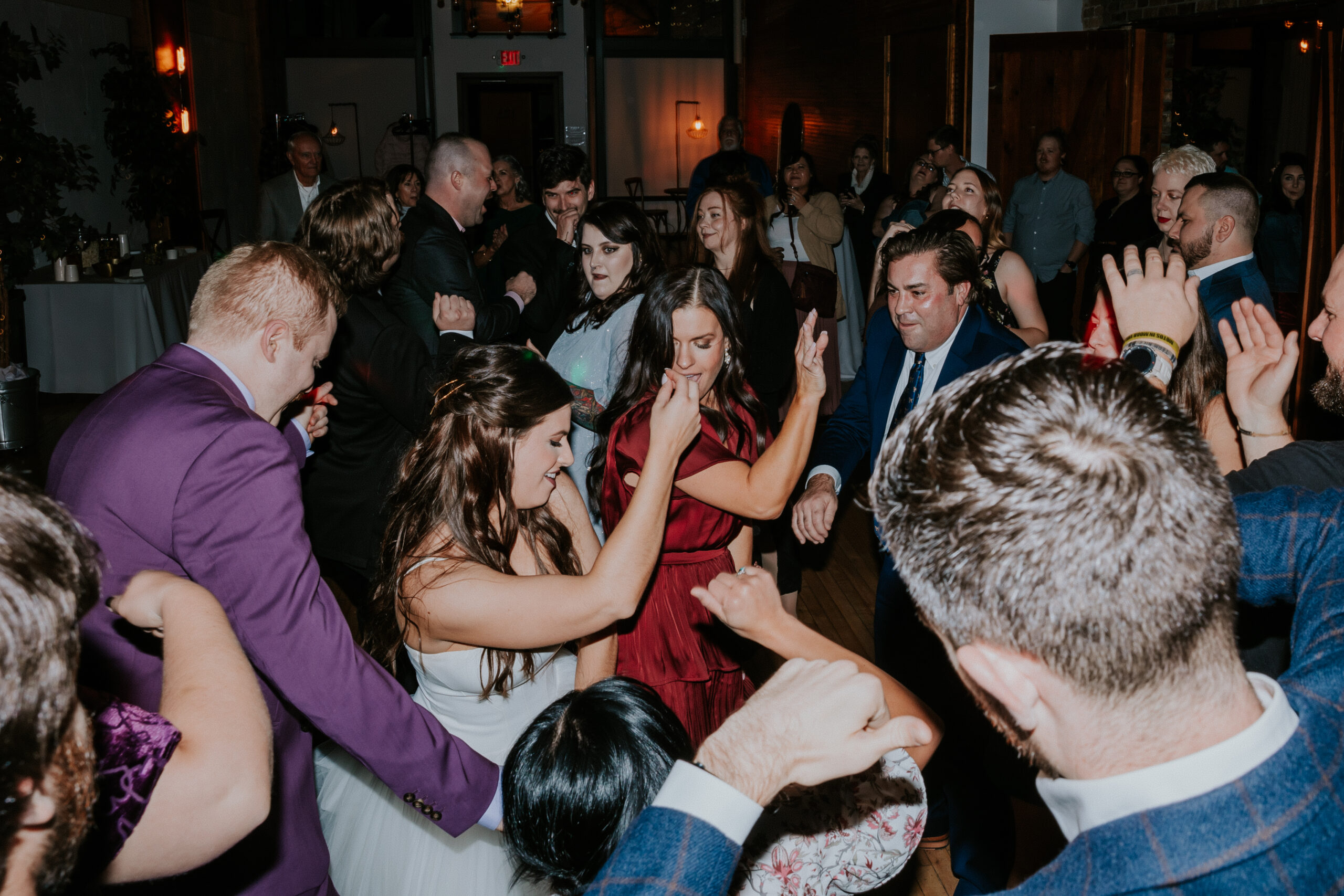 Guests dancing energetically at a packed wedding reception, candid moments captured all around.