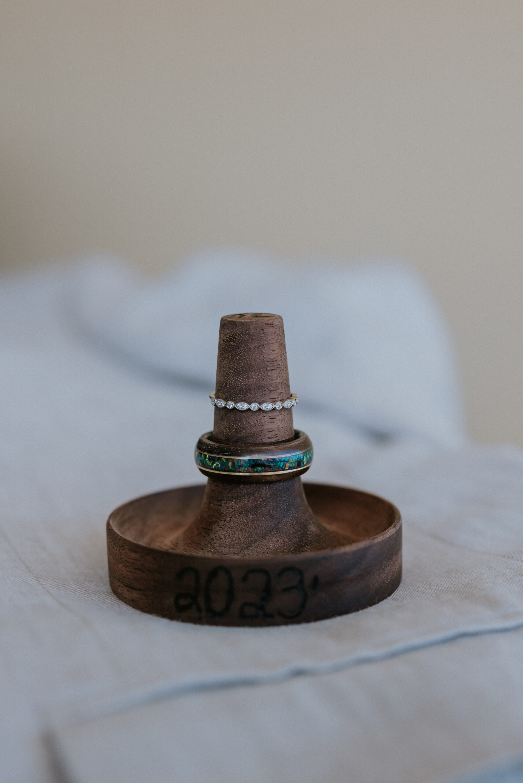 Wedding rings displayed on a wooden holder engraved with the year, a special touch for a beachside ceremony.