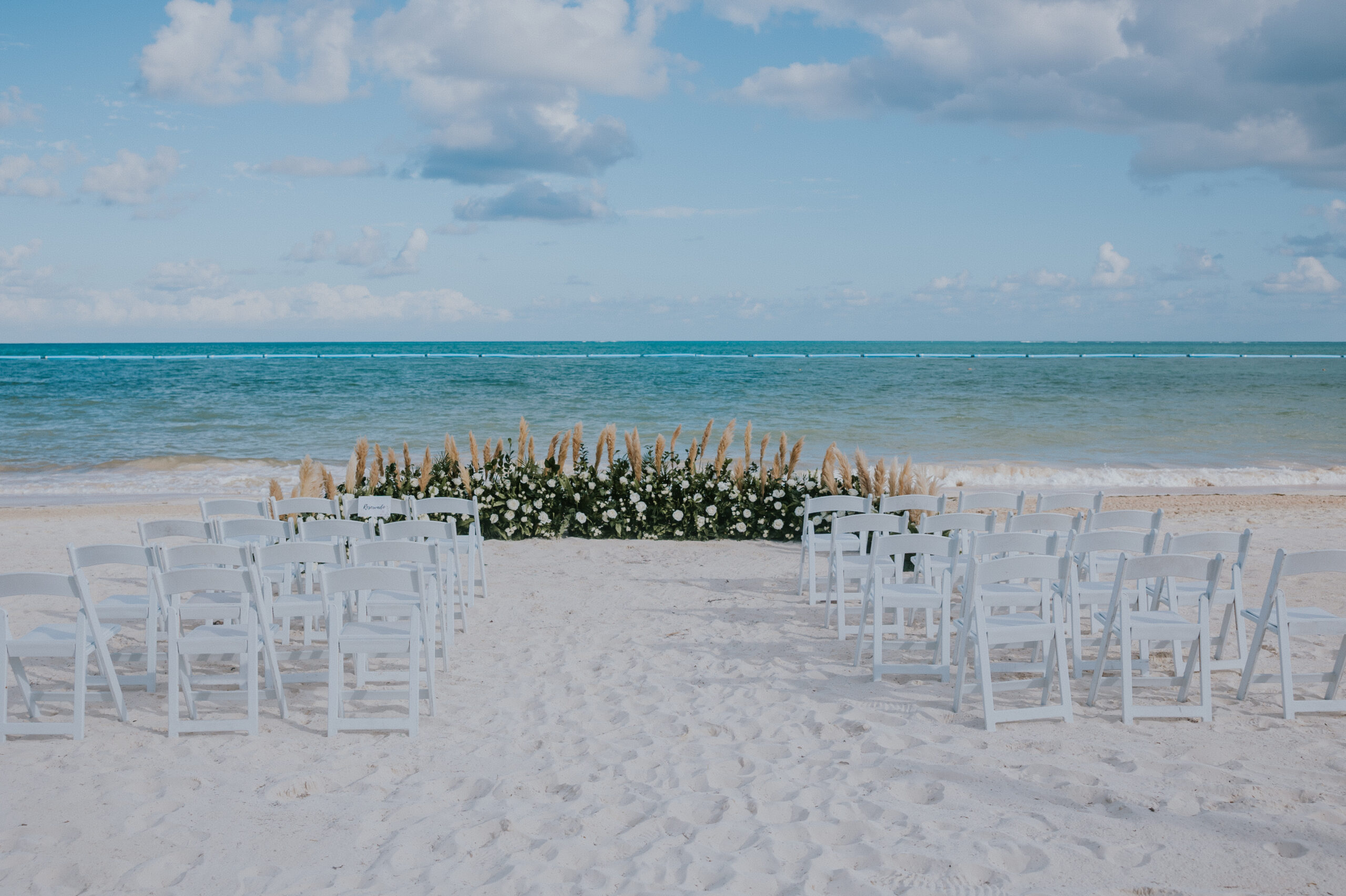 White chairs arranged in rows on the sand, facing a floral altar with sweeping ocean views for a Mexico destination wedding.
