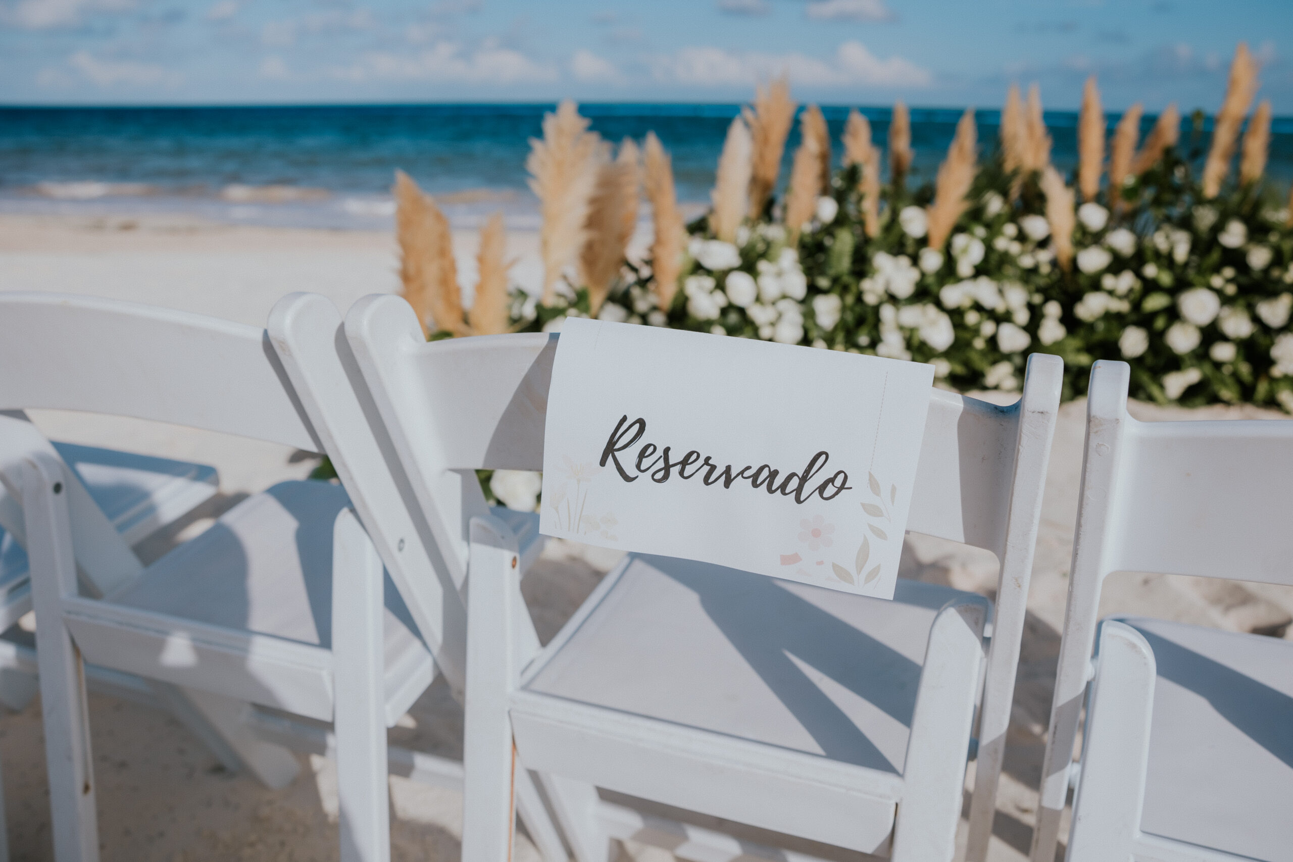 White folding chair with a 'Reservado' sign set up facing the ocean, ready for a Mexico destination wedding ceremony.