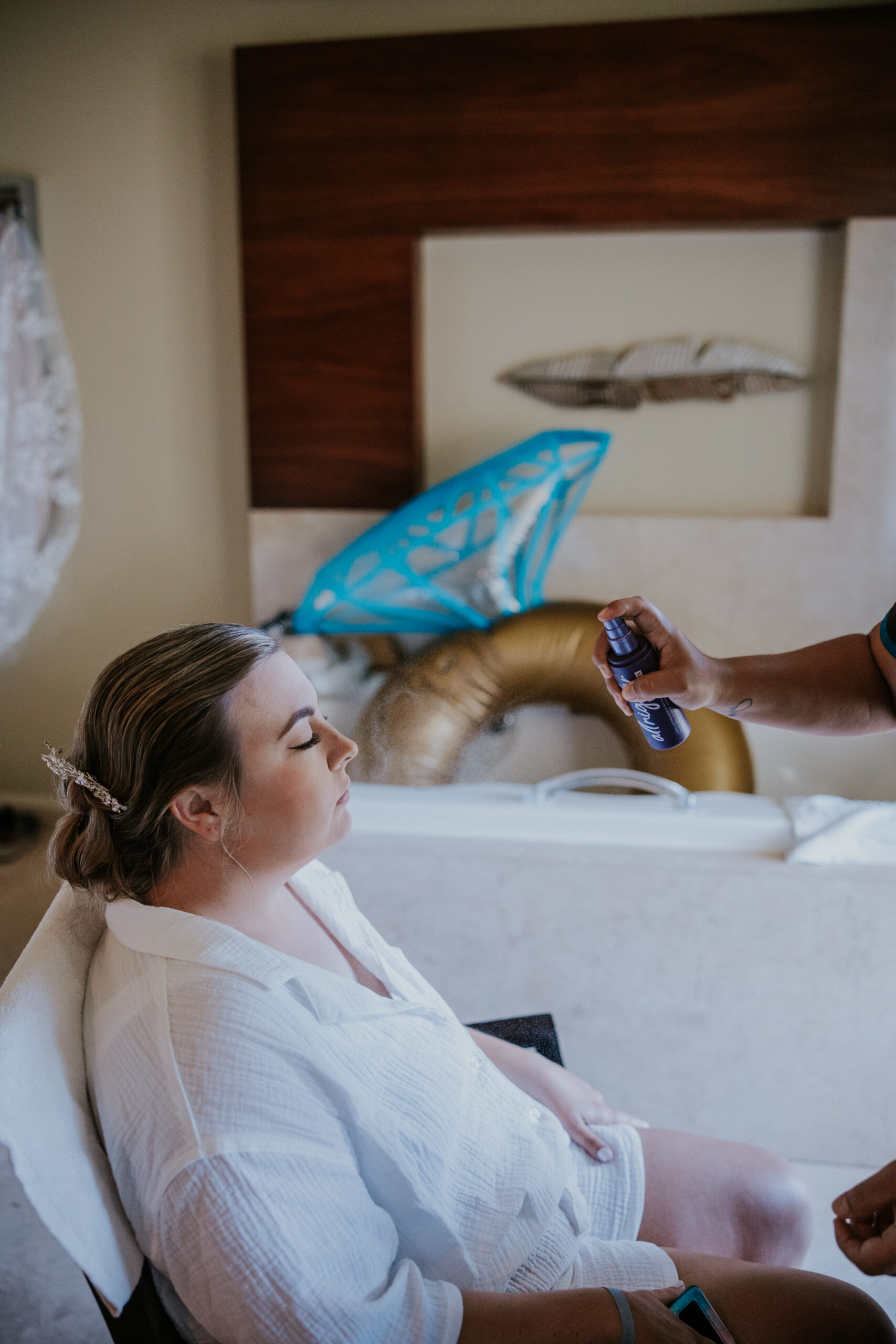 Bride closes her eyes as setting spray is gently applied during makeup prep in the hotel suite.