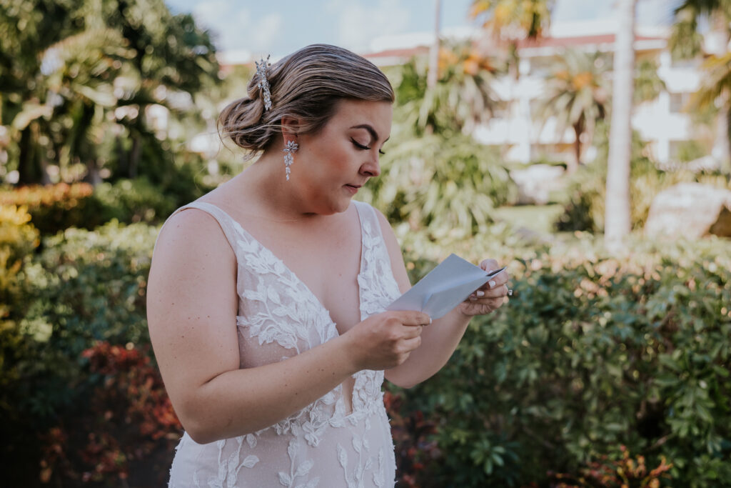 Bride stands in a lush garden setting, reading a handwritten note with emotion just before the ceremony.