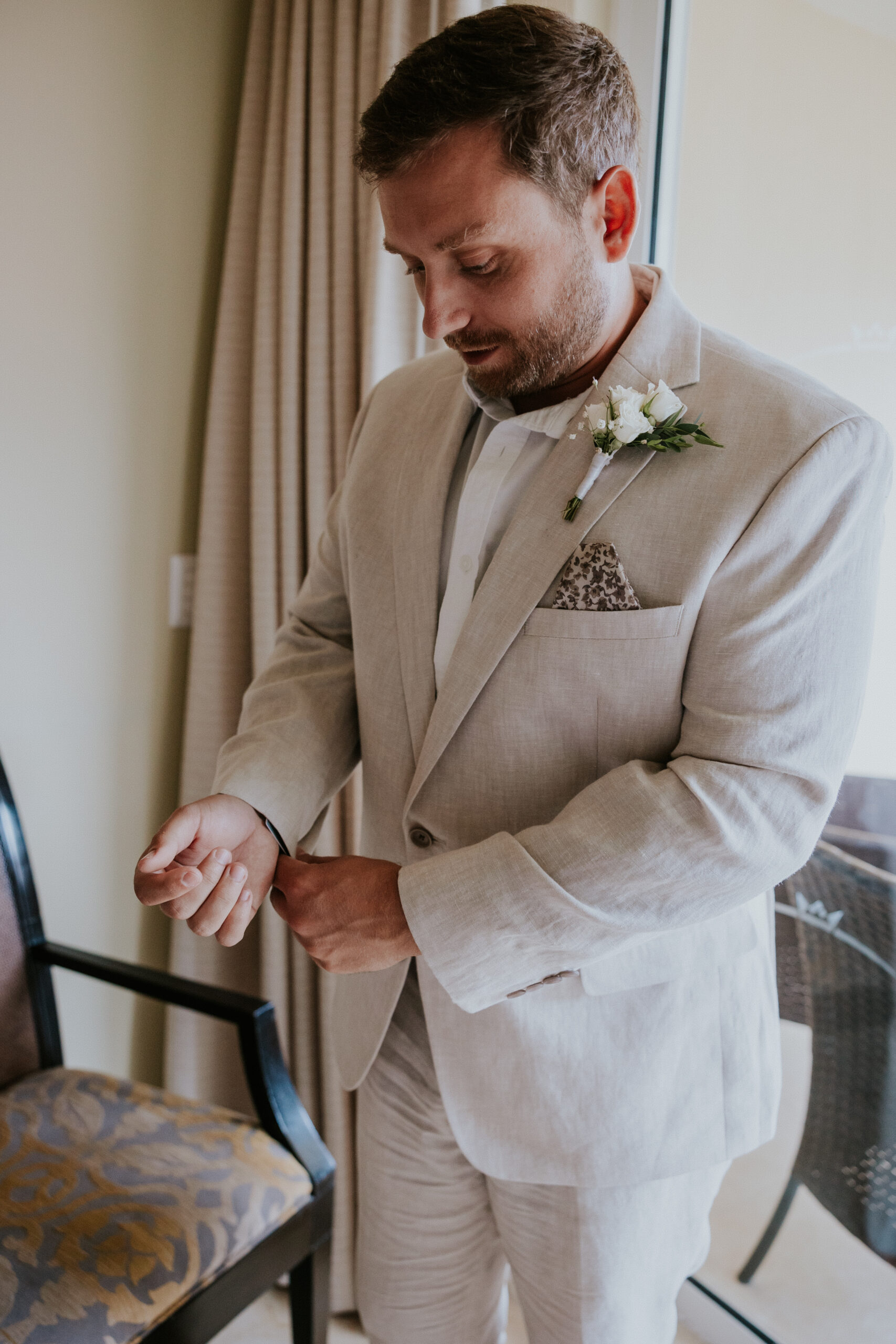 Groom makes final adjustments to his outfit, fixing his cufflinks with a soft smile before the first look.