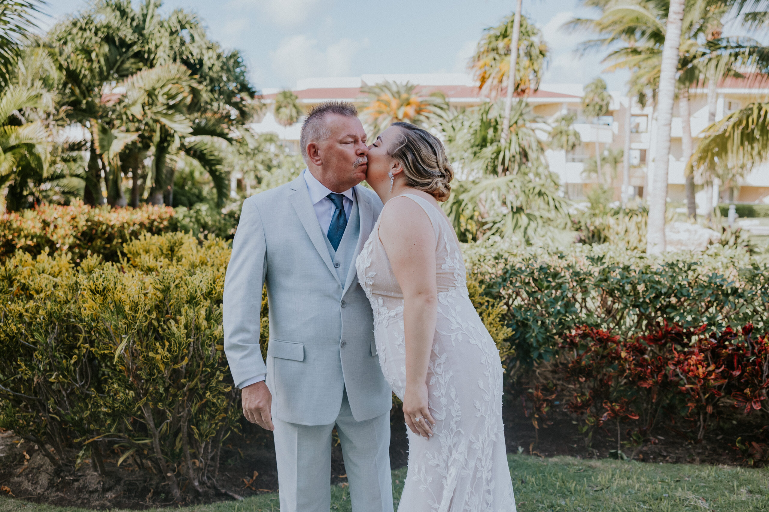 Sweet father-daughter moment as the bride kisses her dad on the cheek in a garden lined with tropical foliage.