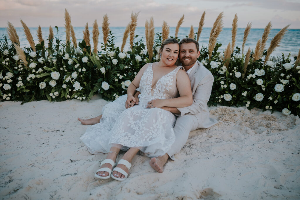 Bride and groom sitting barefoot on the sand surrounded by lush floral arrangements during their Mexico destination wedding.