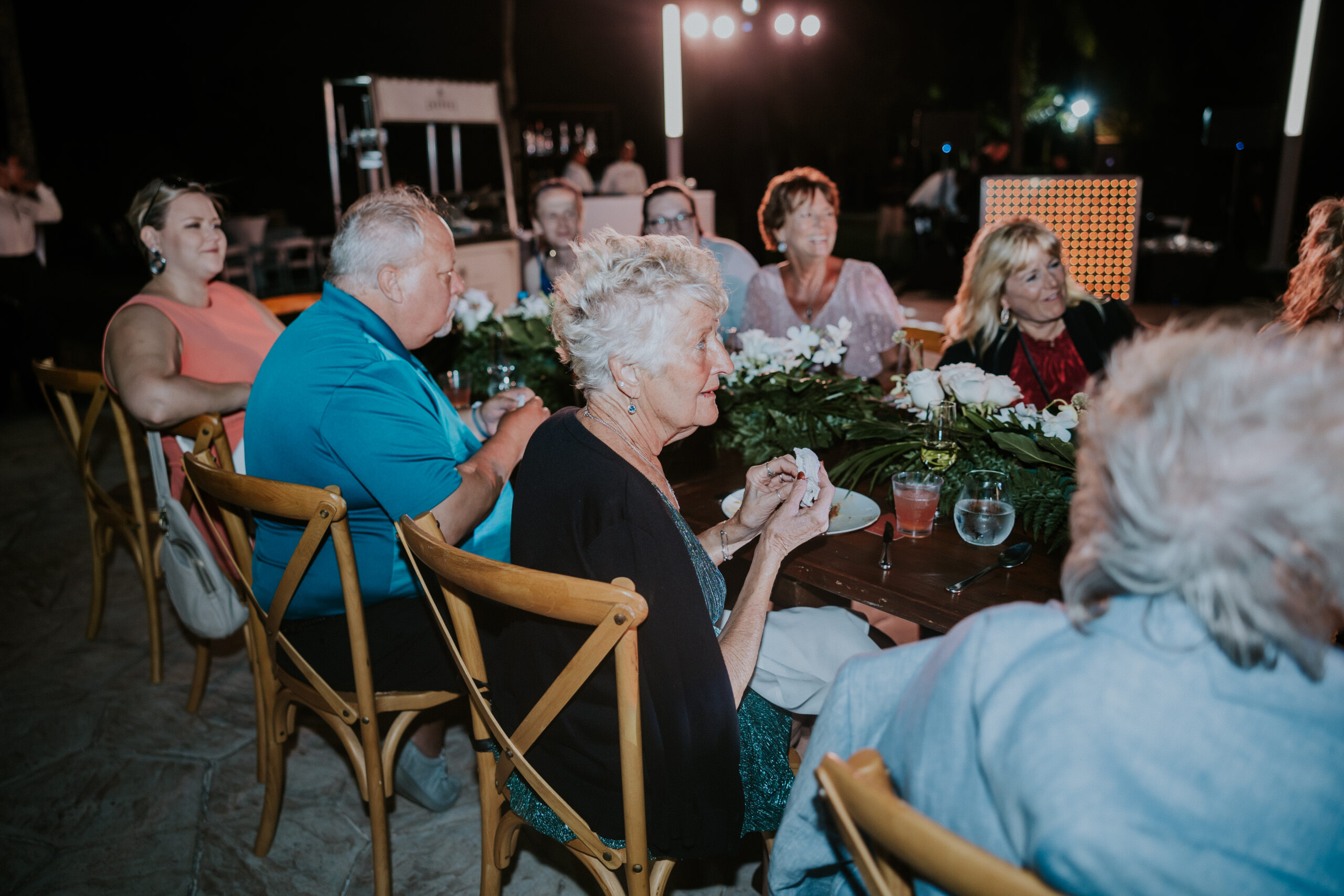 Guests gathered around a long reception table during wedding speeches.