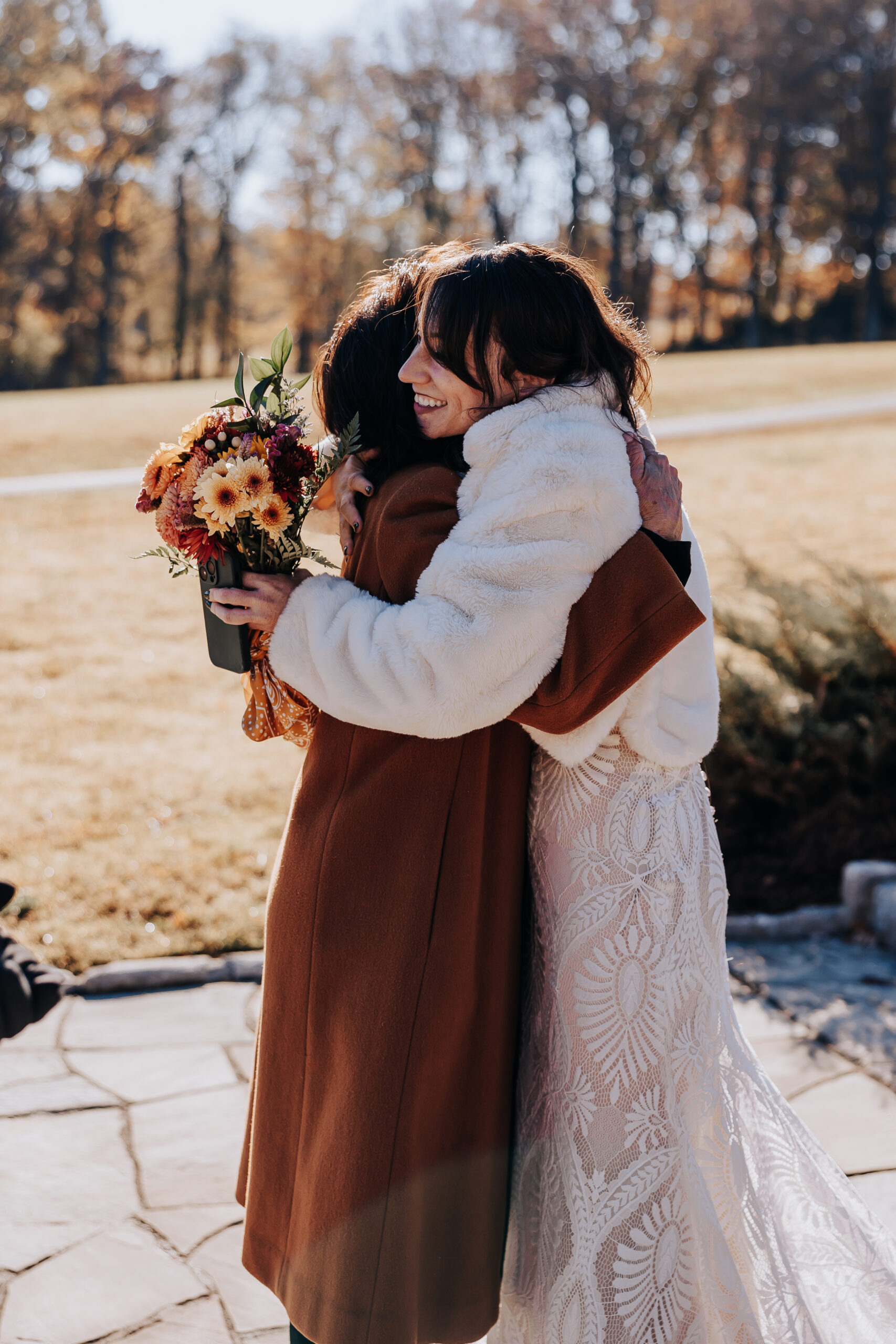 Bride embraces a guest while holding her autumn bouquet, radiating warmth and gratitude after her wedding in Nashville.