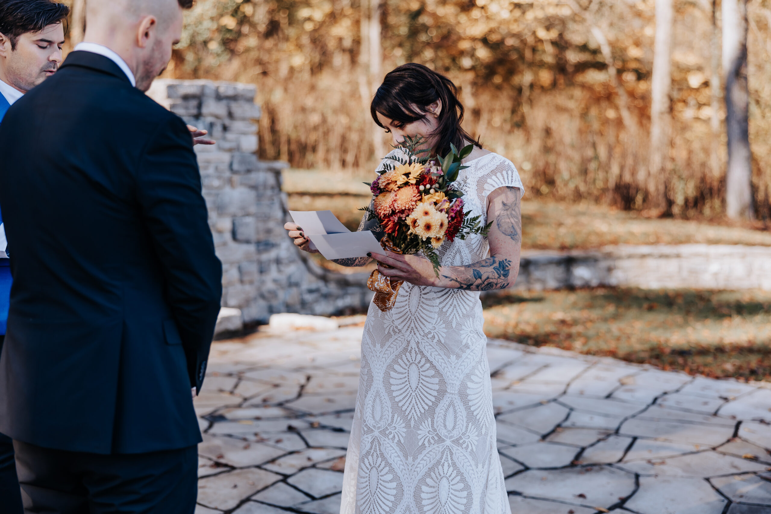 Bride reads heartfelt vows while holding her bouquet, surrounded by loved ones under the golden Tennessee trees.
