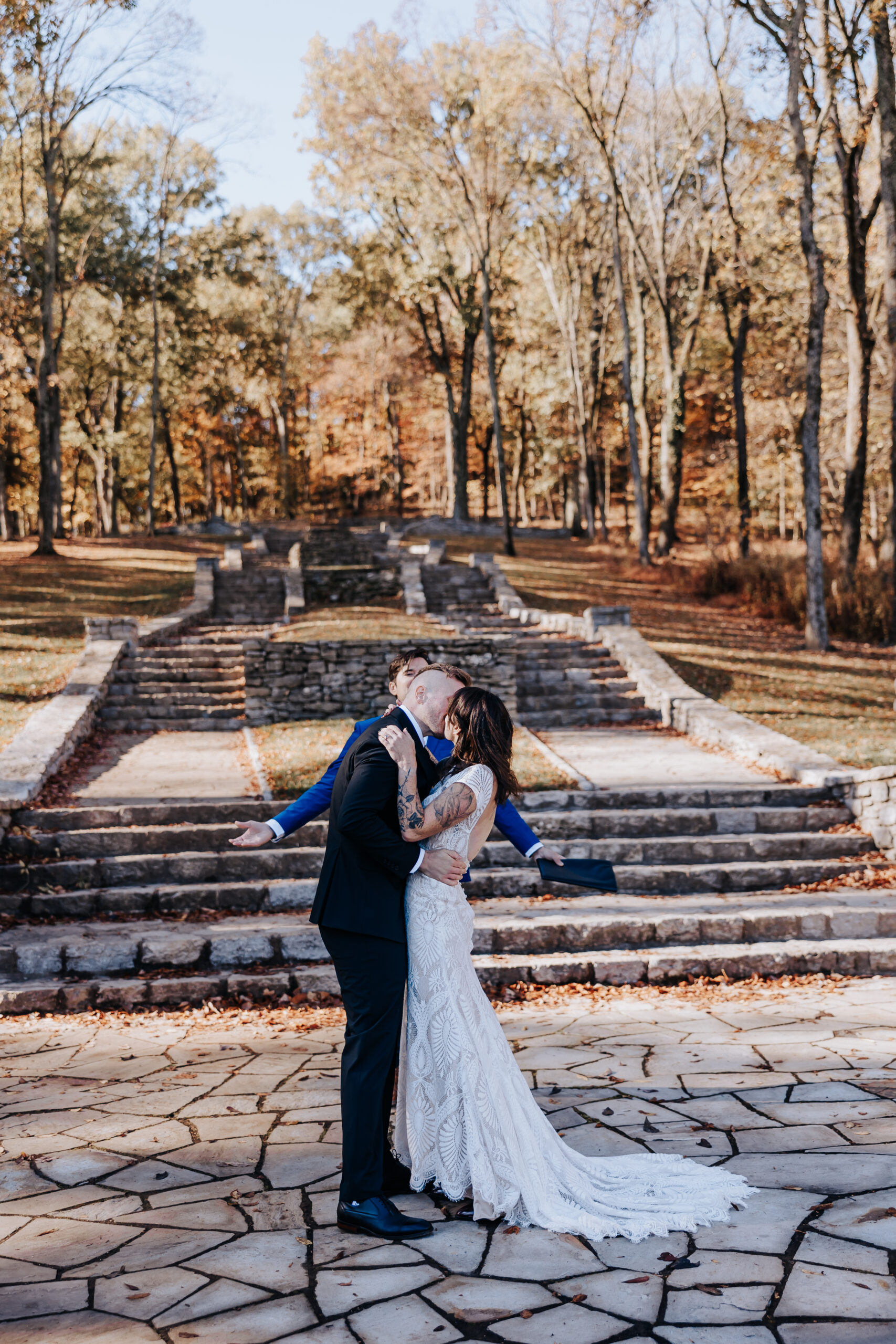 Emotional first kiss as newlyweds in front of the stone amphitheater, leaves scattered around their feet.