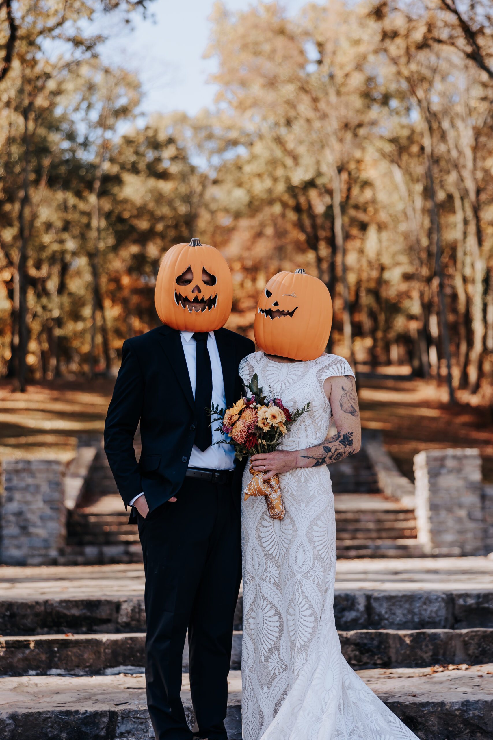 Bride and groom in formal attire with jack-o’-lanterns over their heads, posing on outdoor stone steps during their wedding in Nashville.