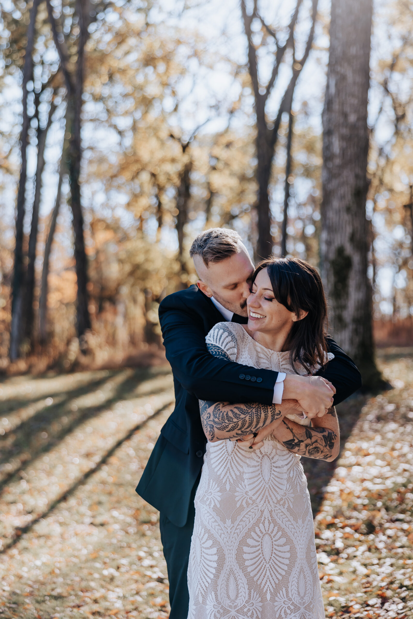 Groom wraps his arms around the smiling bride in a golden autumn forest during their intimate wedding in Nashville.