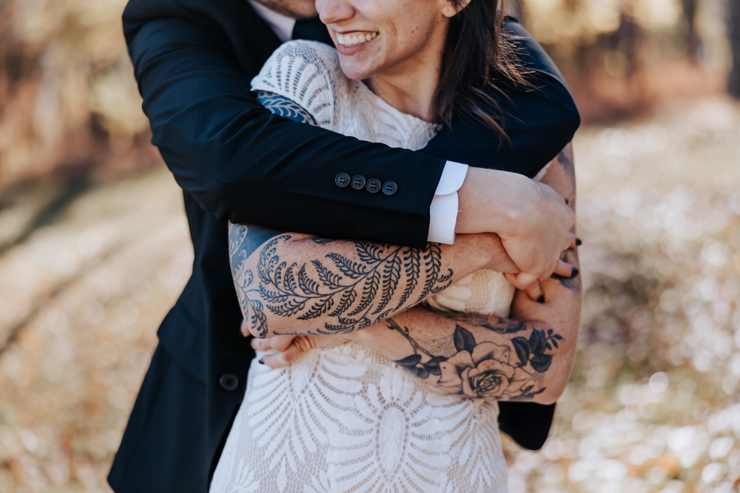 Groom wraps his arms around the bride, showing her detailed floral tattoos and lace gown during their wedding in Nashville.
