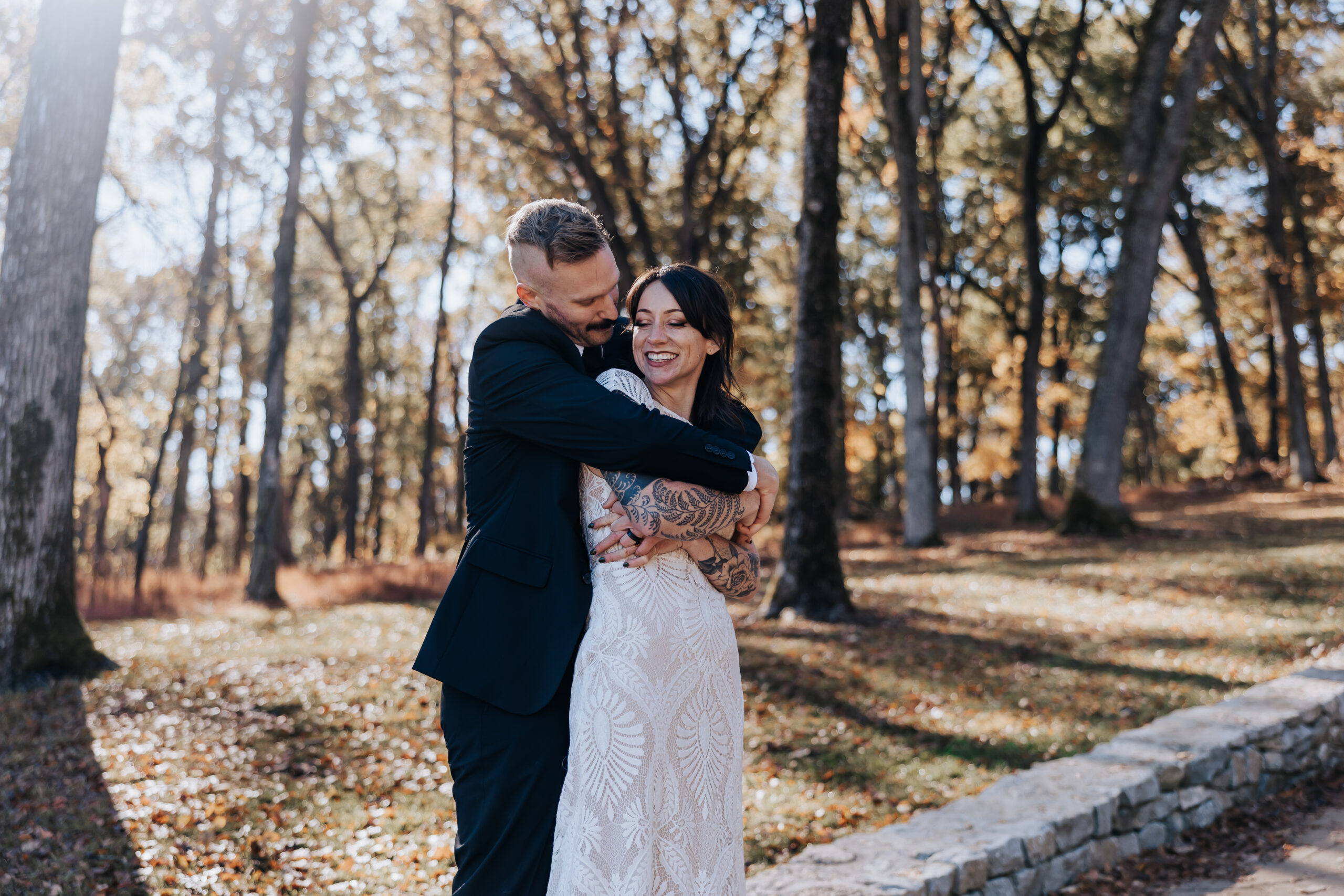 Groom hugs the bride from behind under sun-dappled trees, both glowing with post-ceremony joy at their wedding in Nashville.