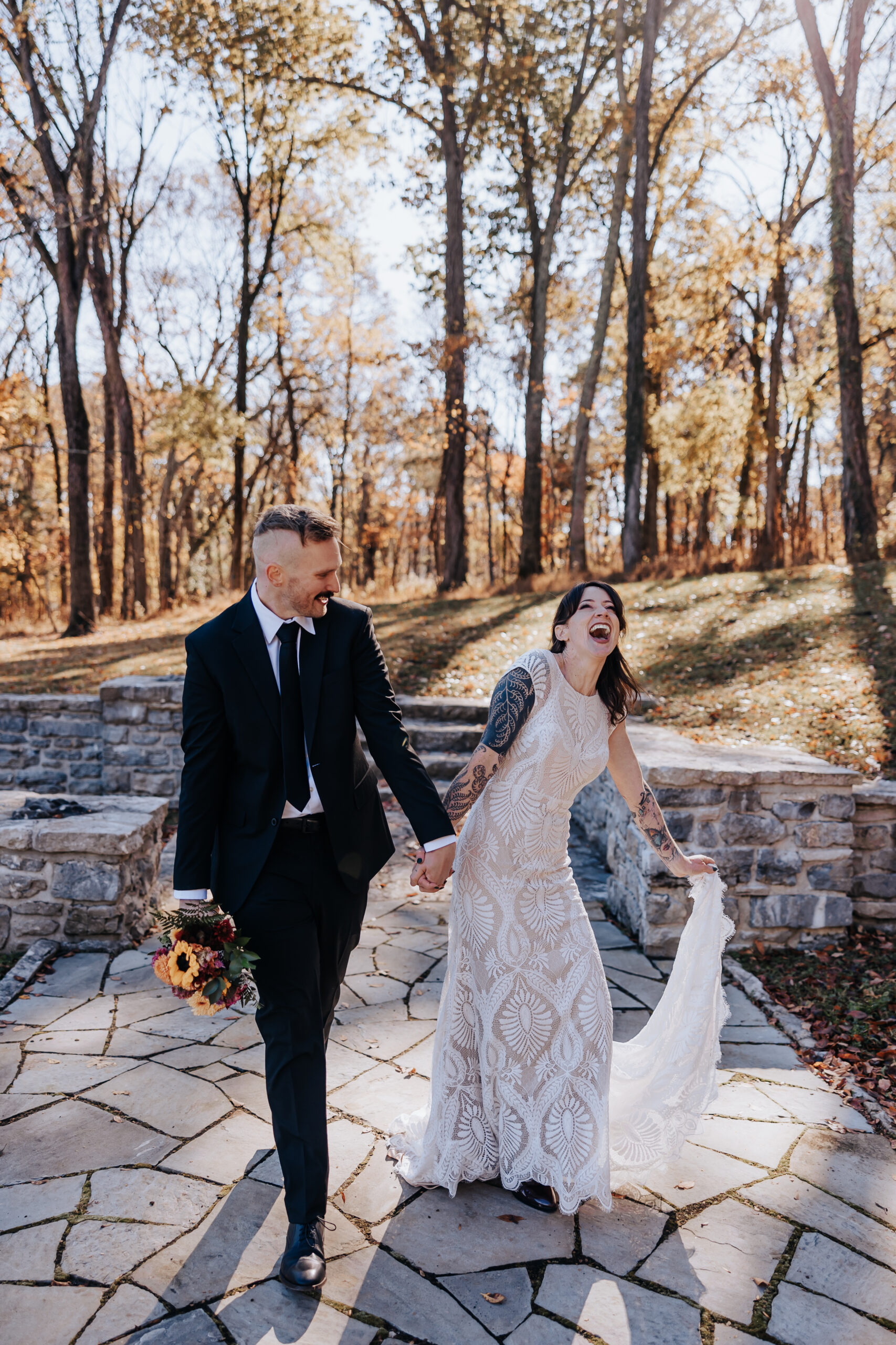 Bride and groom walk hand-in-hand down a stone path, laughing joyfully during their fall wedding in Nashville.