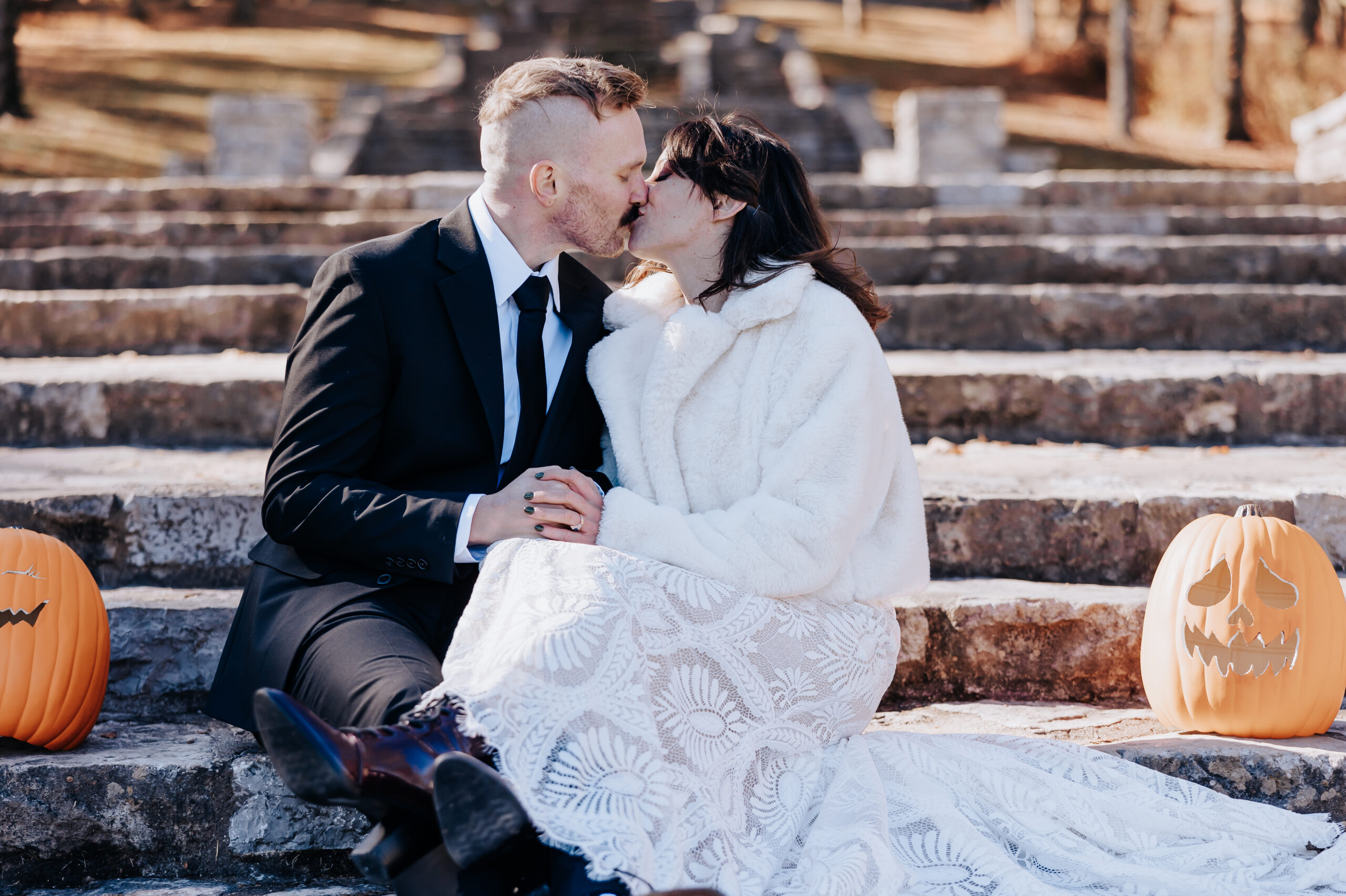 Cozy and romantic moment as newlyweds kiss on stone steps, framed by carved pumpkins at their wedding in Nashville.