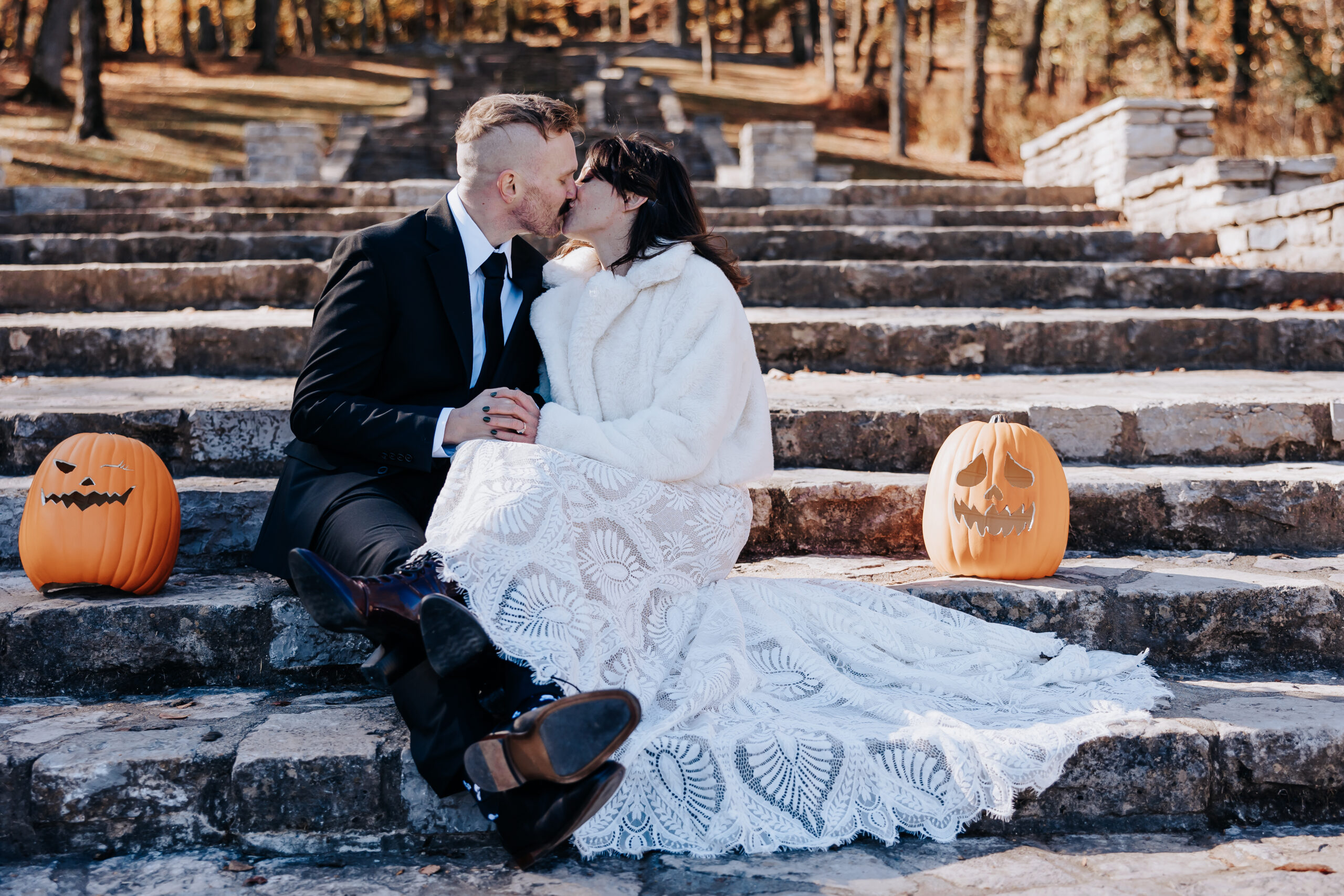 Bride and groom kiss while sitting on stone steps, surrounded by carved pumpkins during their playful fall wedding in Nashville.