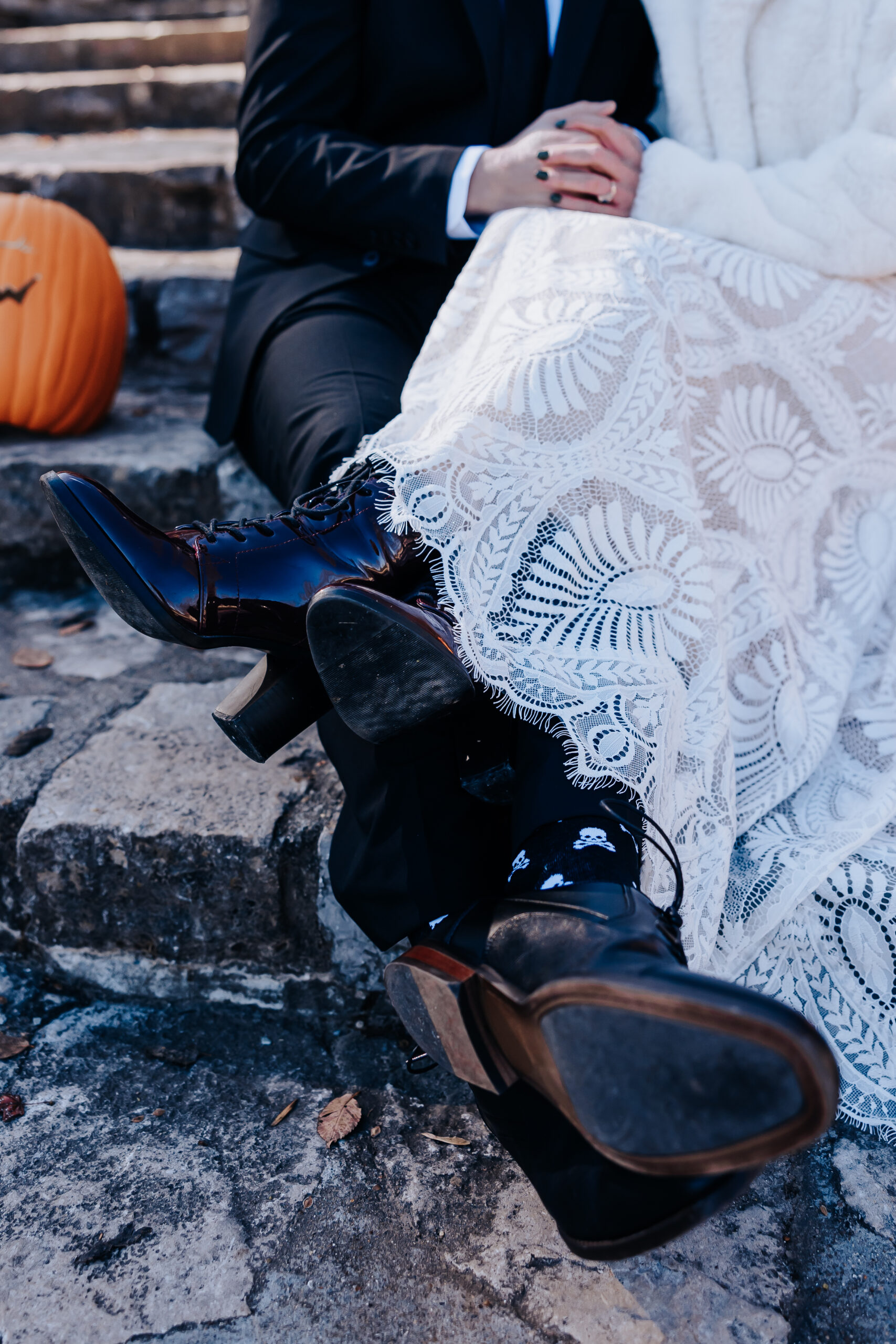 Close-up of lace wedding dress and vintage-style boots resting on stone steps, with a hint of autumn leaves and pumpkins.