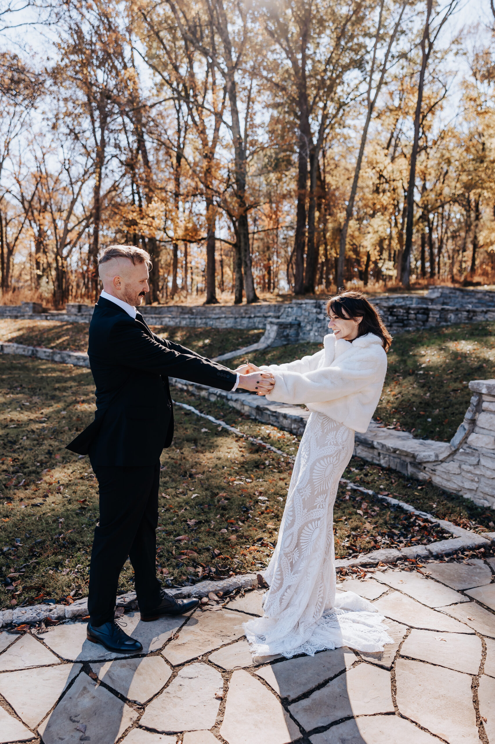 Couple holds hands and smiles at each other on a crisp autumn day, wrapped in love and golden light.