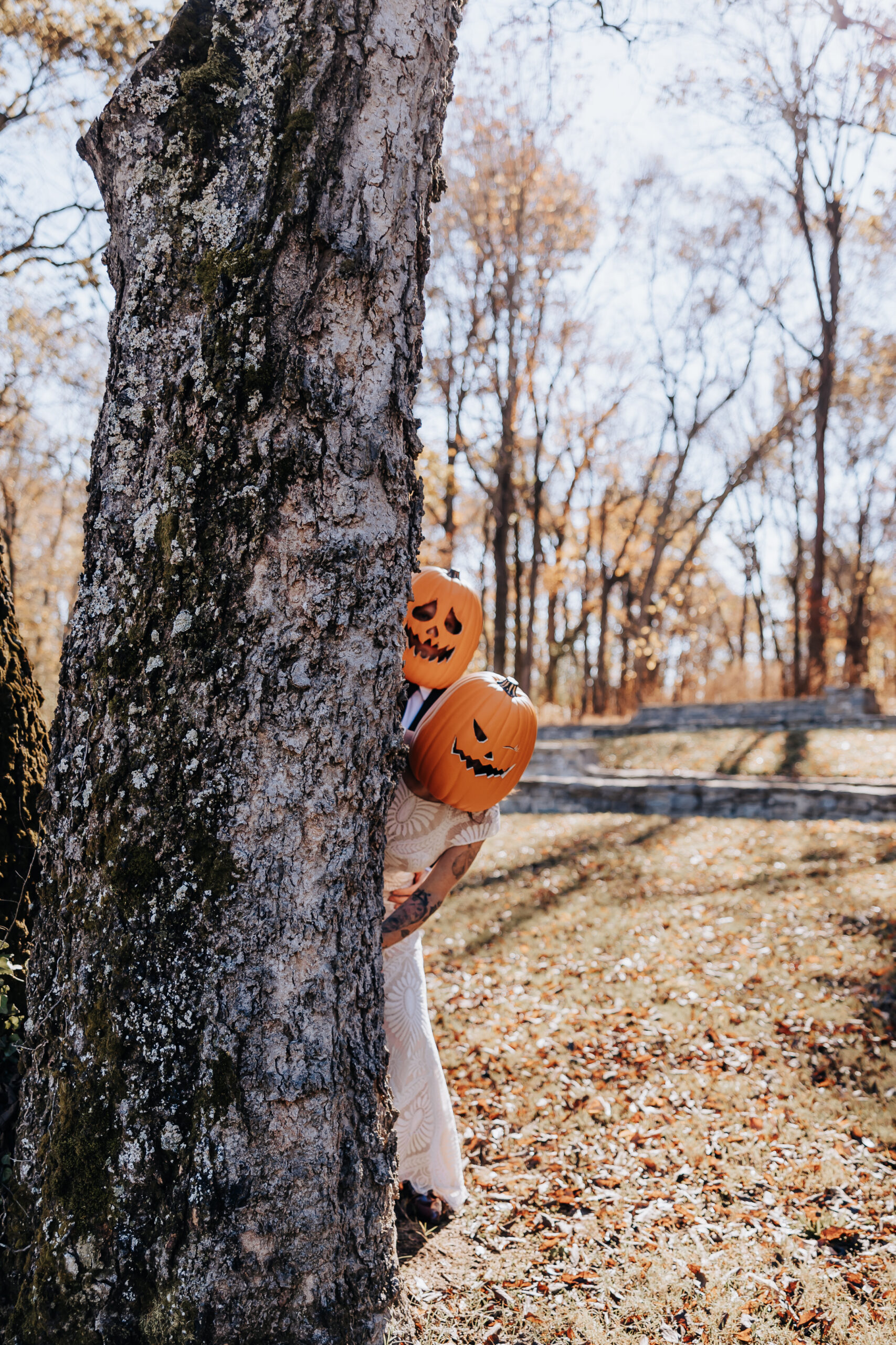 Couple wearing pumpkin masks playfully peeks out from behind a tree, adding Halloween fun to their wedding in Nashville.