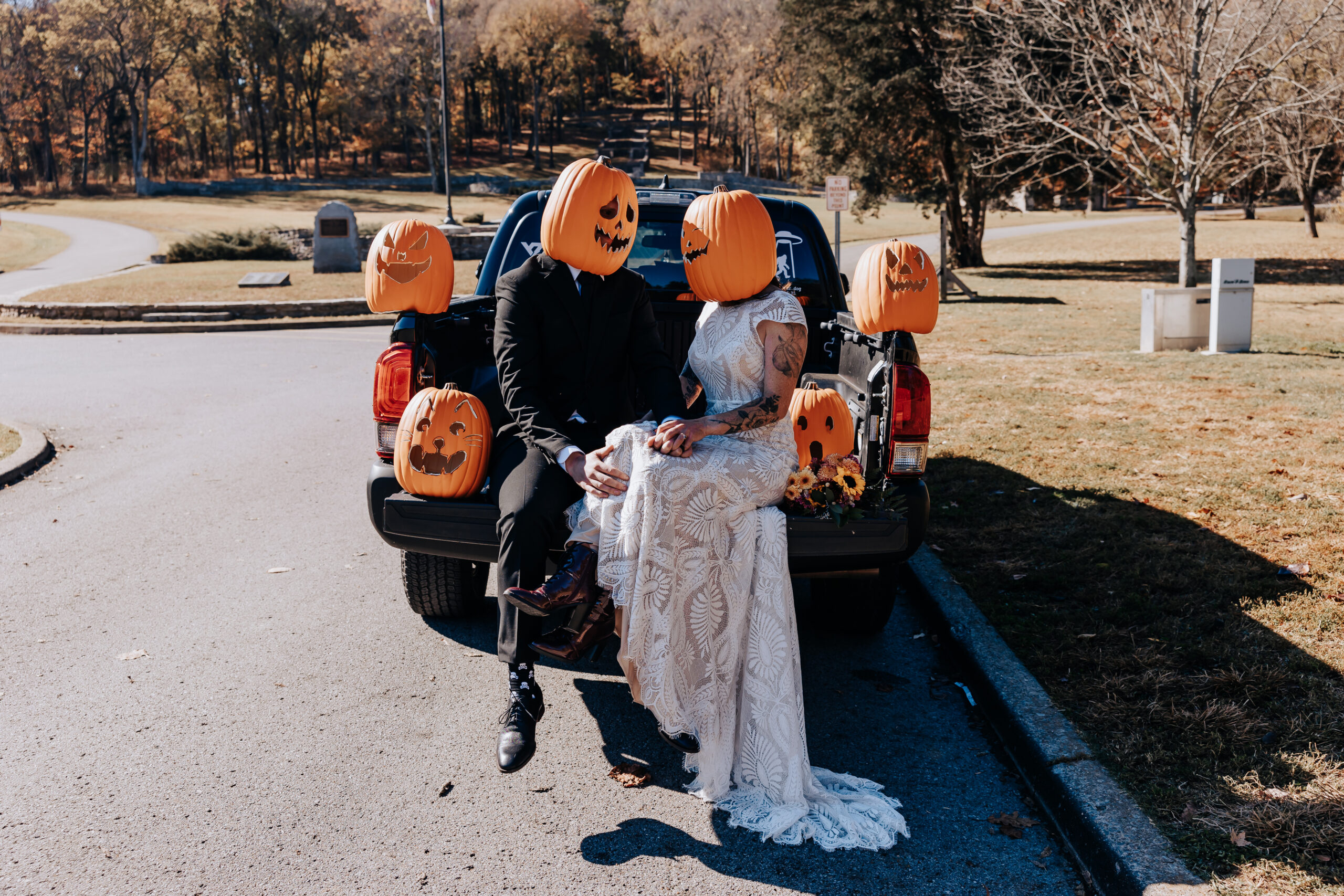 Bride and groom sit on the tailgate in pumpkin masks, showing off their fun Halloween-inspired wedding vibes.
