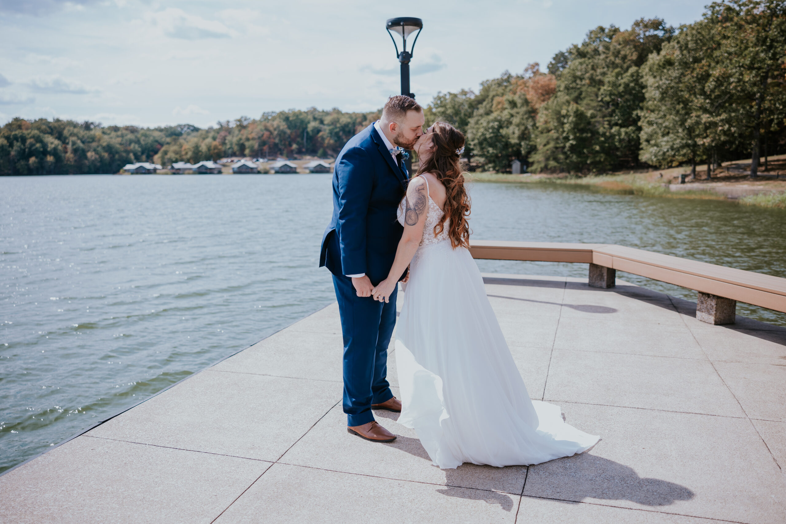 Romantic kiss on a lakeside dock, framed by calm waters and wooded hills — a dreamy scene inspired by unique wedding ideas in the heart of Tennessee.