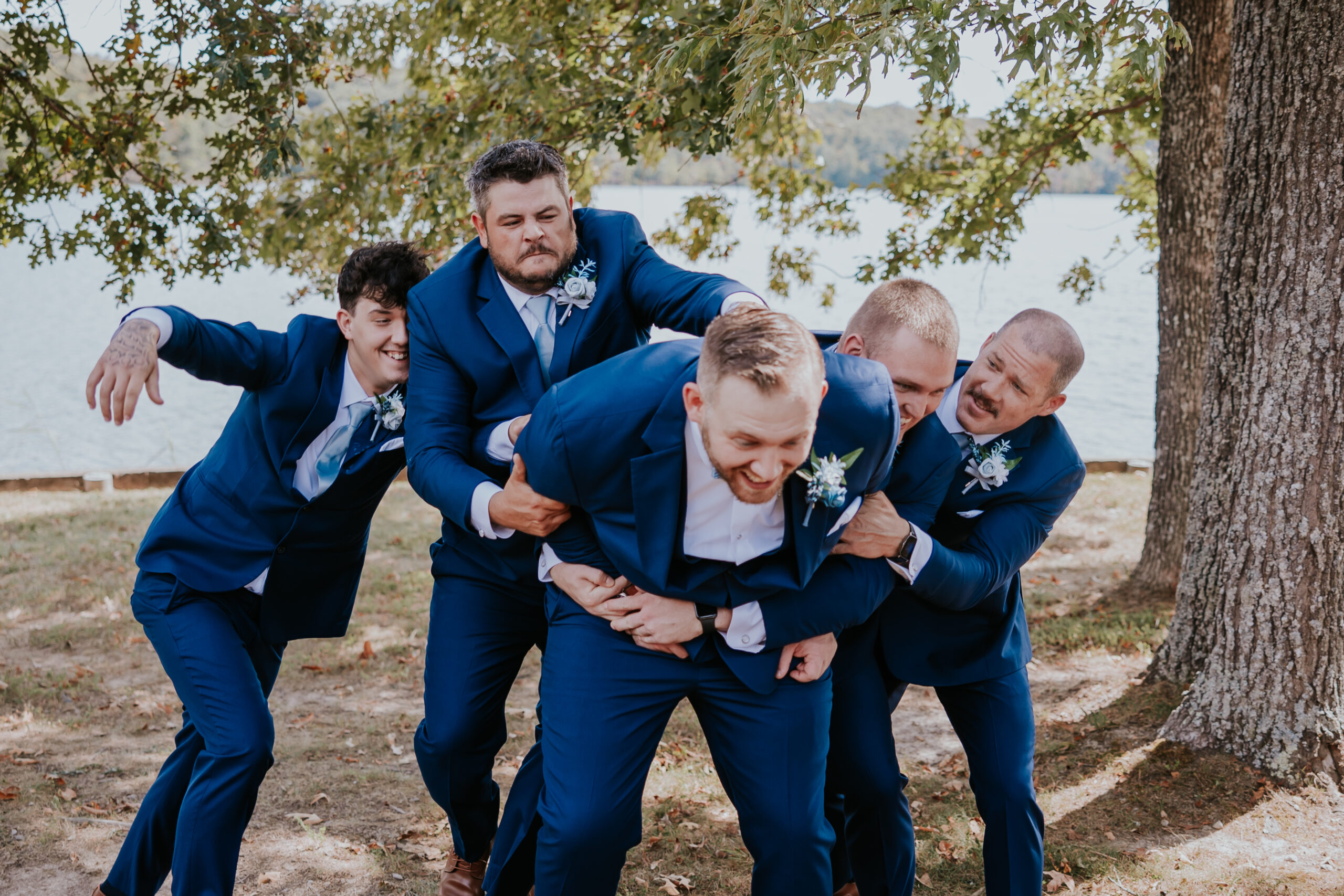 Groomsmen playfully pile onto the groom for a fun moment by the lake, capturing the joy and brotherhood behind the big day.