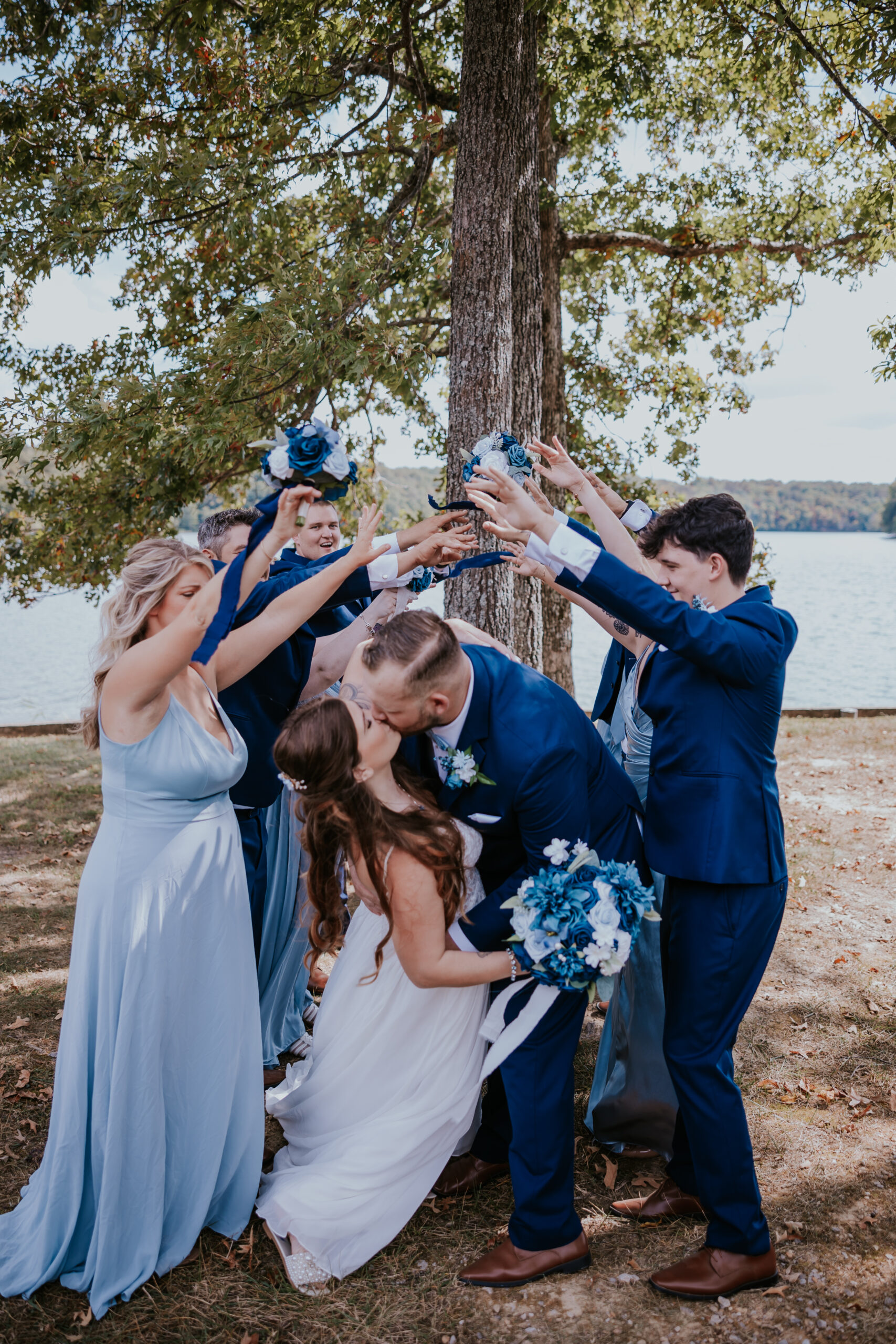 The wedding party cheers as the newlyweds kiss beneath a tunnel of raised arms, showing off playful and unique wedding ideas for group portraits.