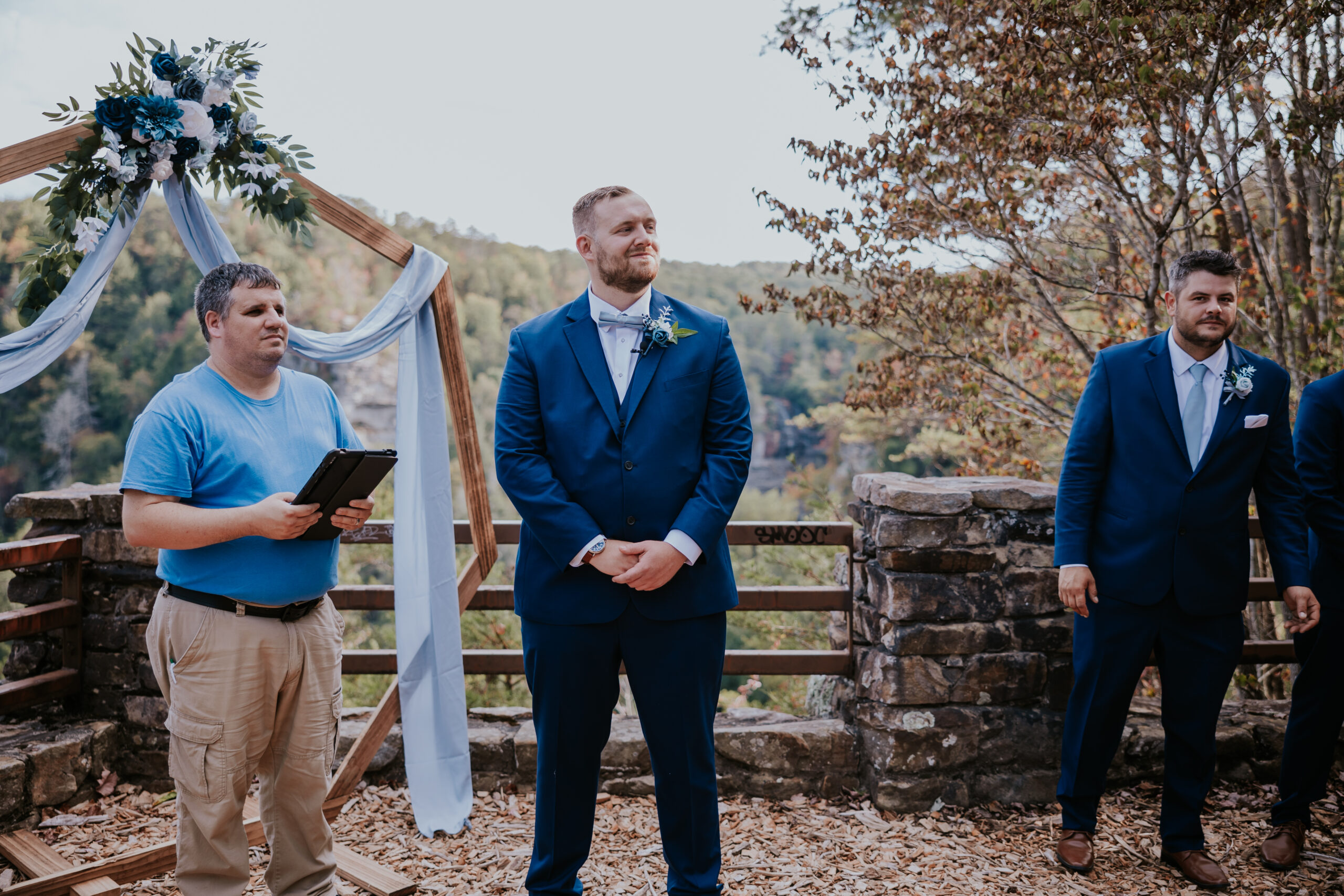 Groom stands at the altar with a smile, eagerly awaiting his bride with a breathtaking overlook behind him.