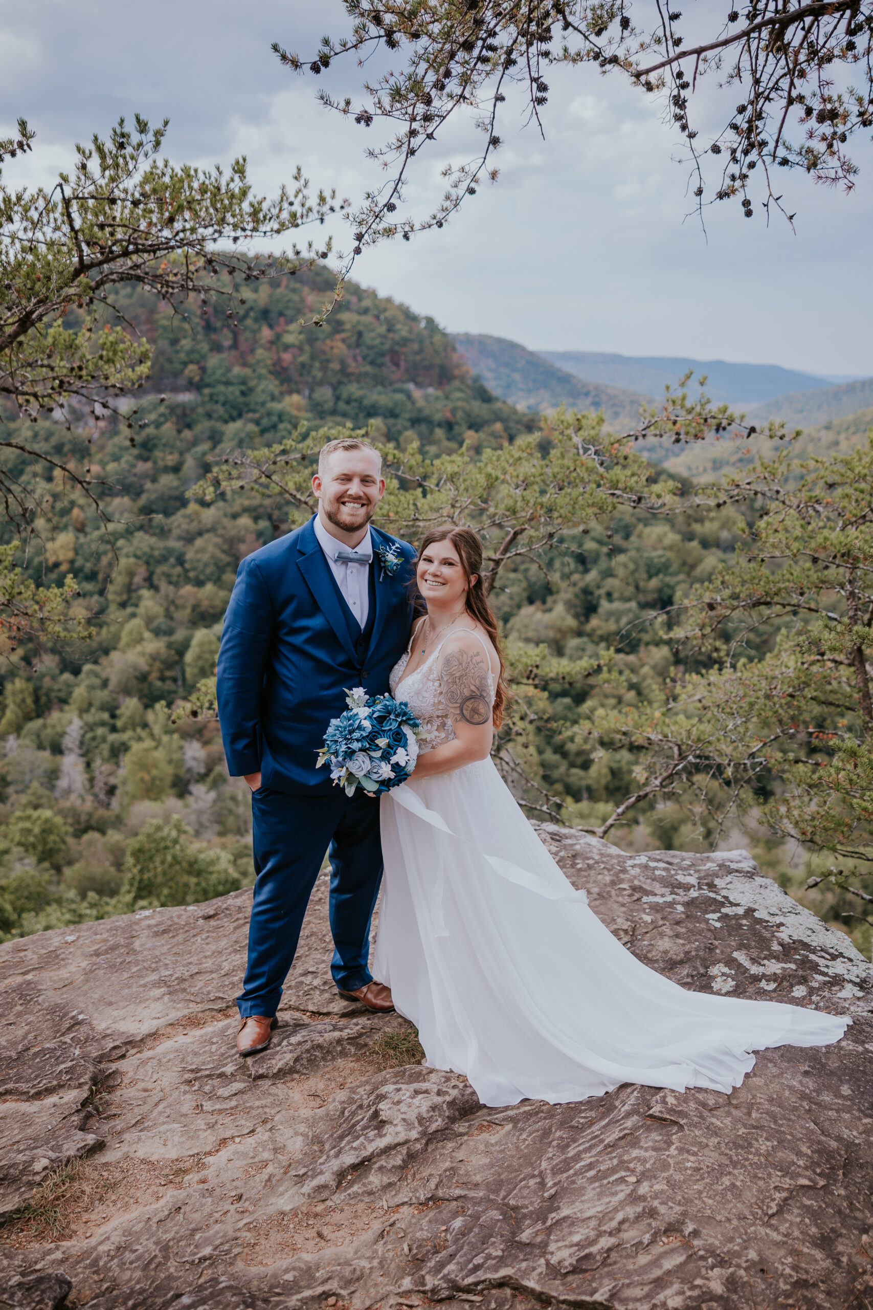 Newlyweds smiling at the camera while standing on a cliff edge at Fall Creek Falls — a joyful portrait that highlights unique wedding ideas for Tennessee elopements.