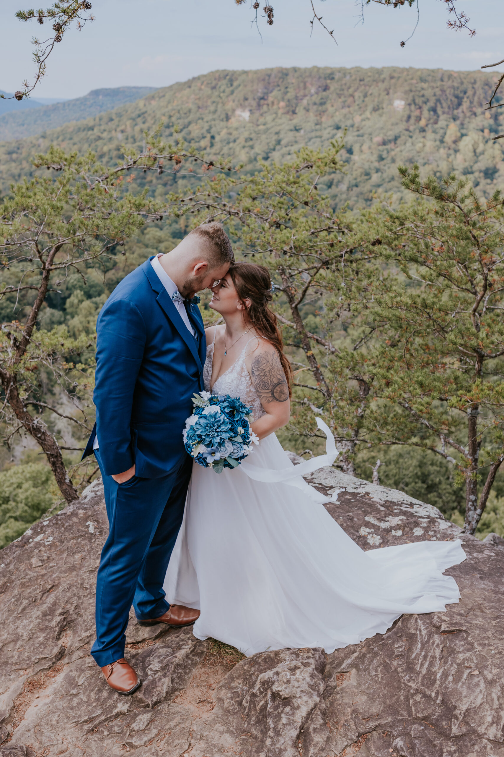 Couple standing on a dramatic cliff edge, the bride holding a blue bouquet — a beautiful example of unique wedding ideas for adventurous couples.