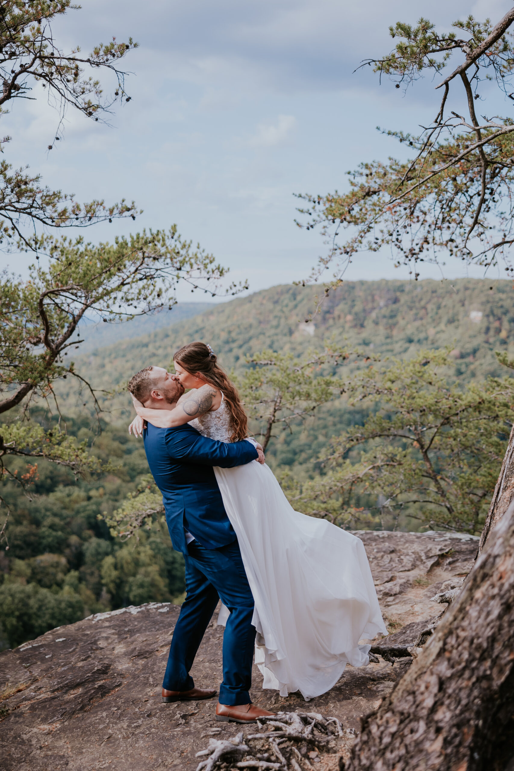 The groom lifts the bride in a joyful embrace on a mountain ledge, capturing one of many unique wedding ideas perfect for nature lovers.