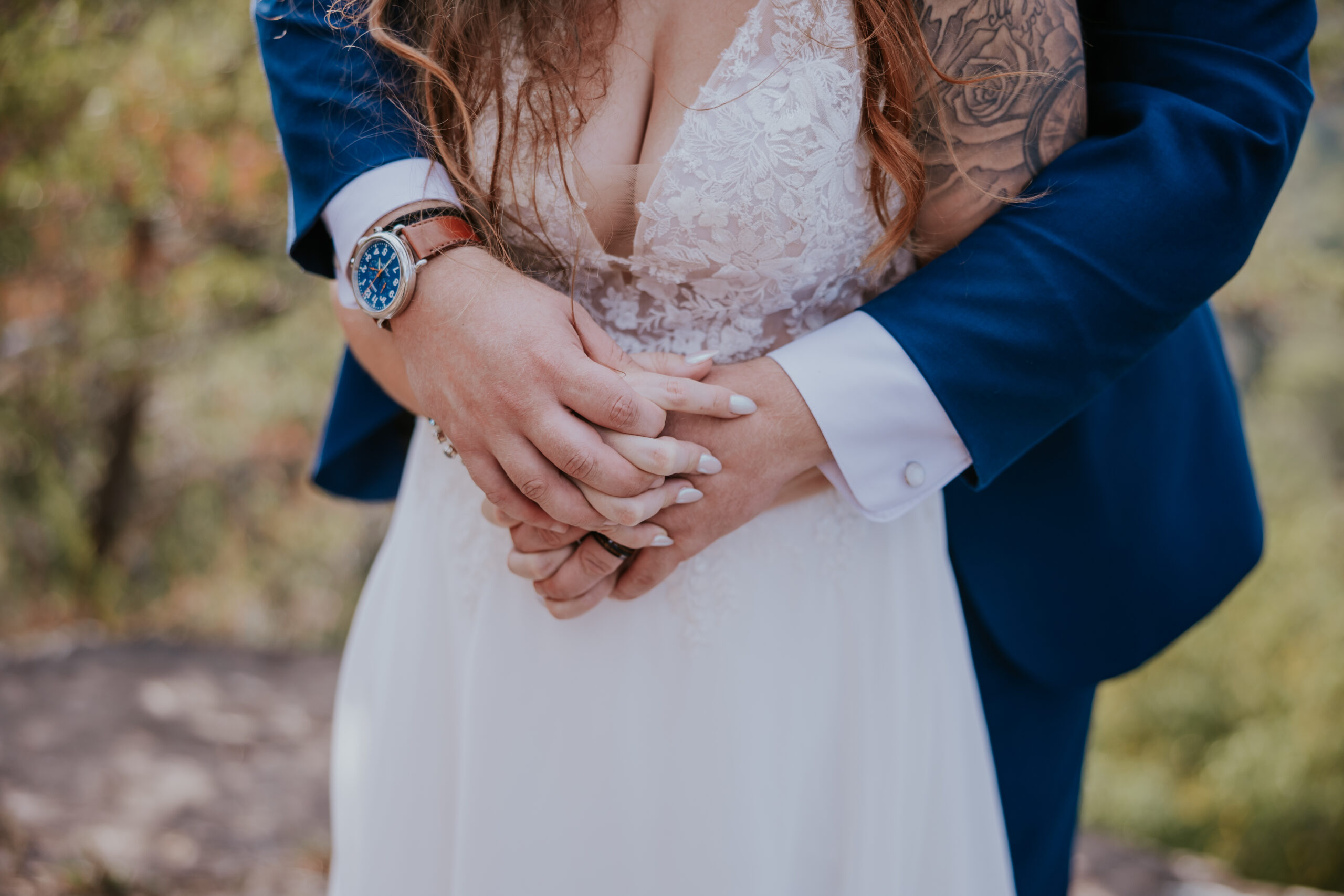 Close-up of the groom’s arms wrapped around the bride’s waist, highlighting their wedding bands and the bride’s lace bodice.
