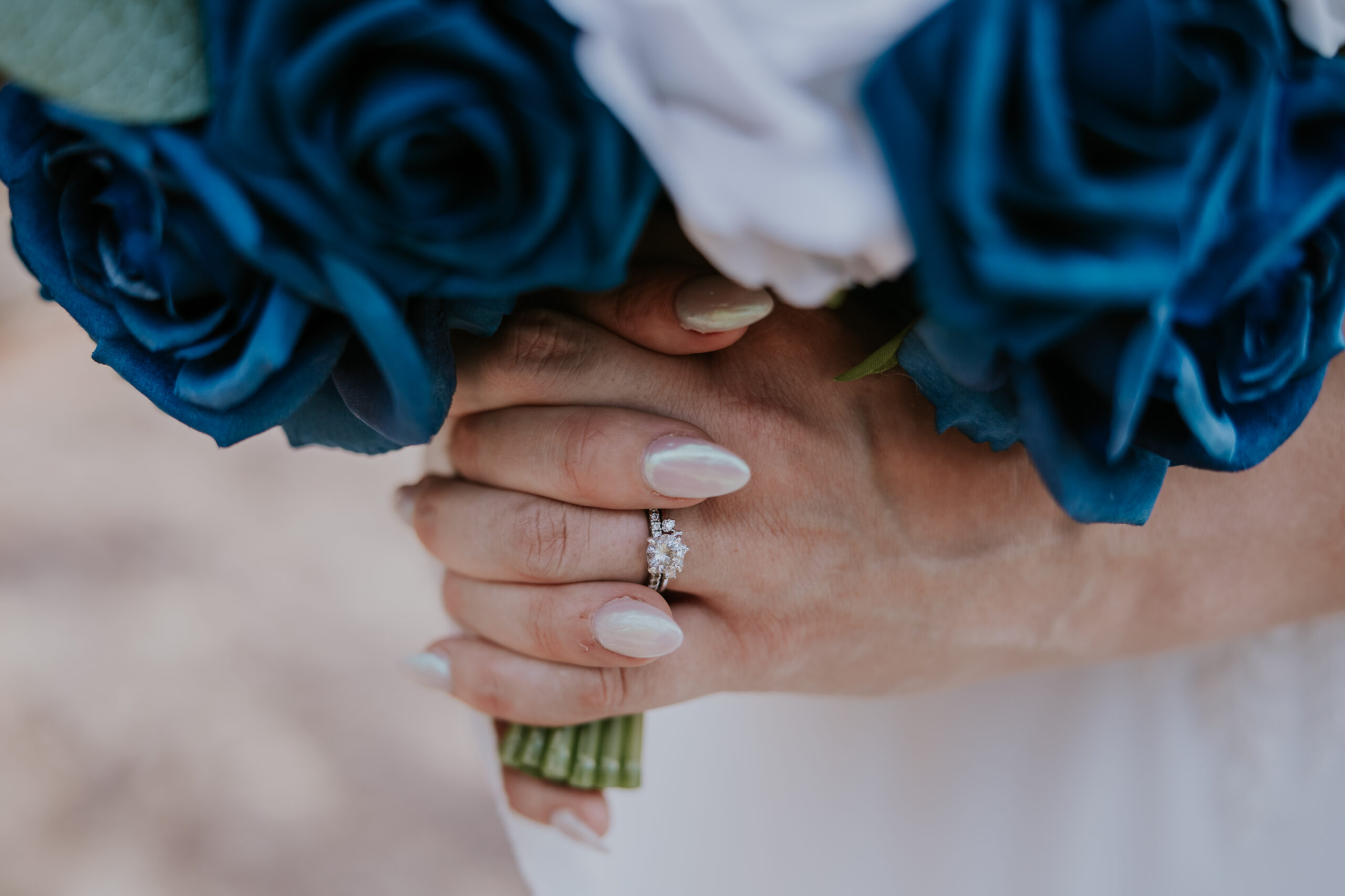Detailed shot of the bride’s engagement ring and pearl nails as she clutches a blue and white rose bouquet — a small but stunning touch in their collection of unique wedding ideas.
