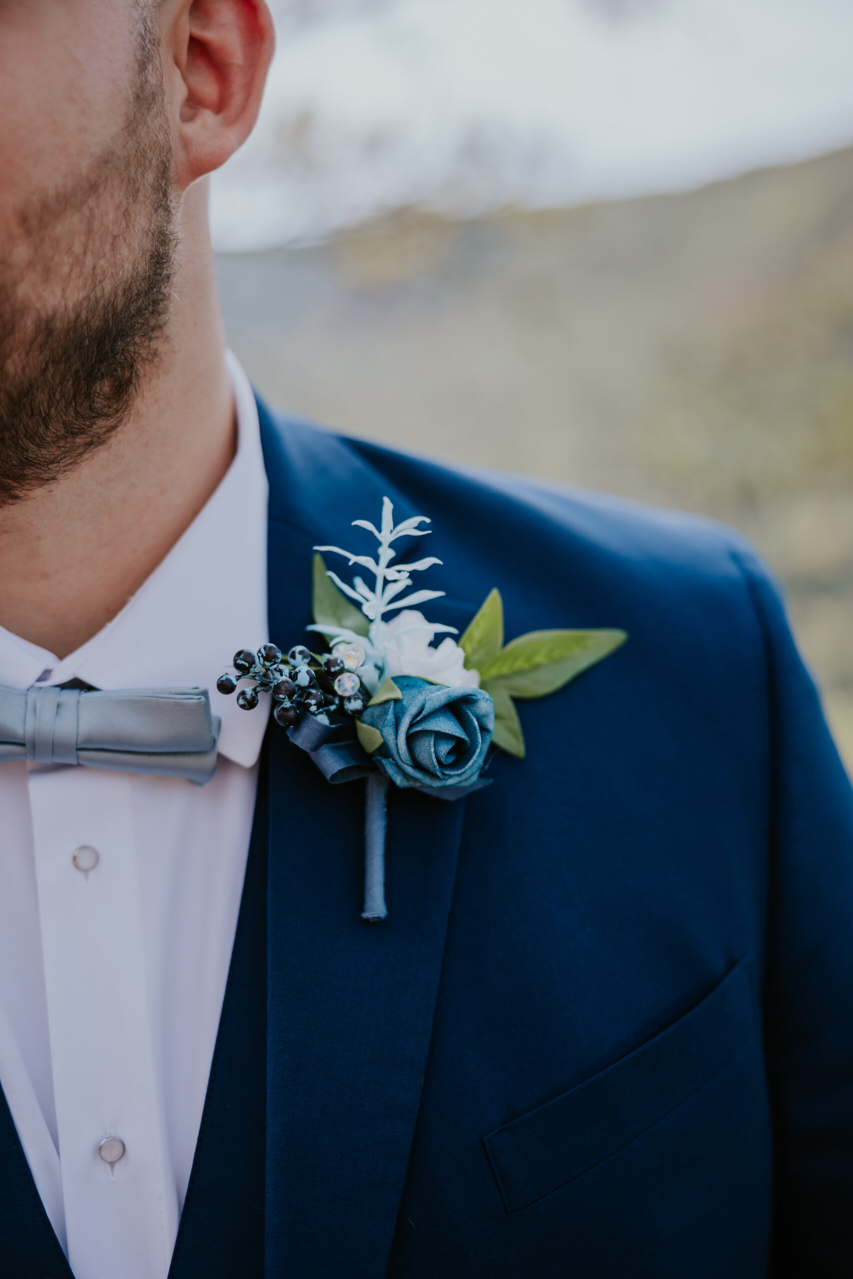 Close-up of the groom’s navy suit and blue boutonnière with greenery and white accents, styled to match the mountain wedding aesthetic.