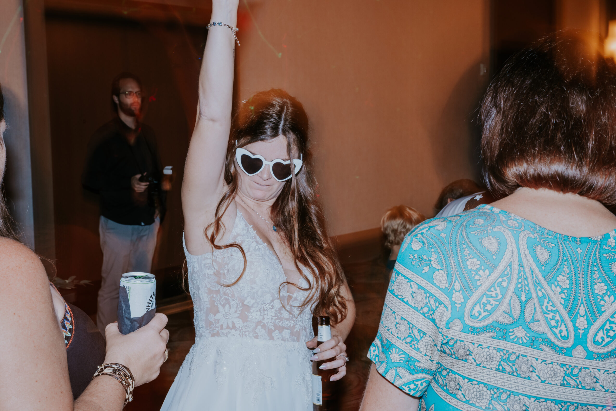Bride dancing in heart-shaped sunglasses, arm raised in celebration — a playful twist on traditional reception vibes and a nod to unique wedding ideas.