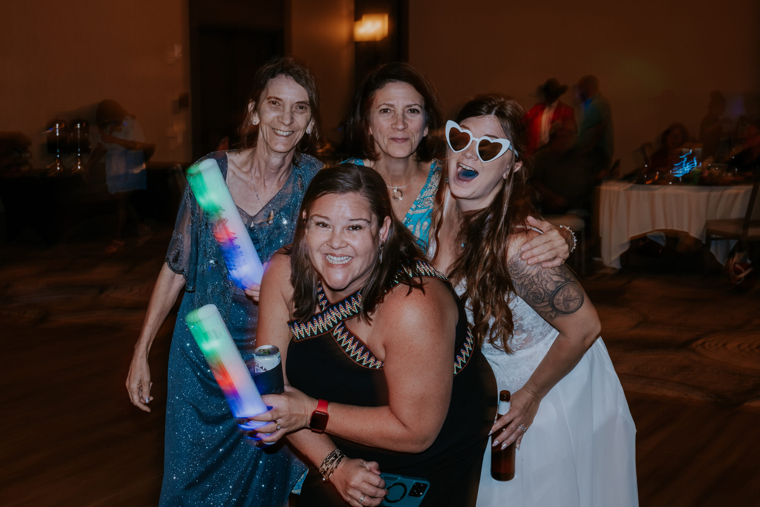 The bride and her friends laugh with glow sticks and drinks in hand, celebrating with unique wedding ideas that keep the party alive.