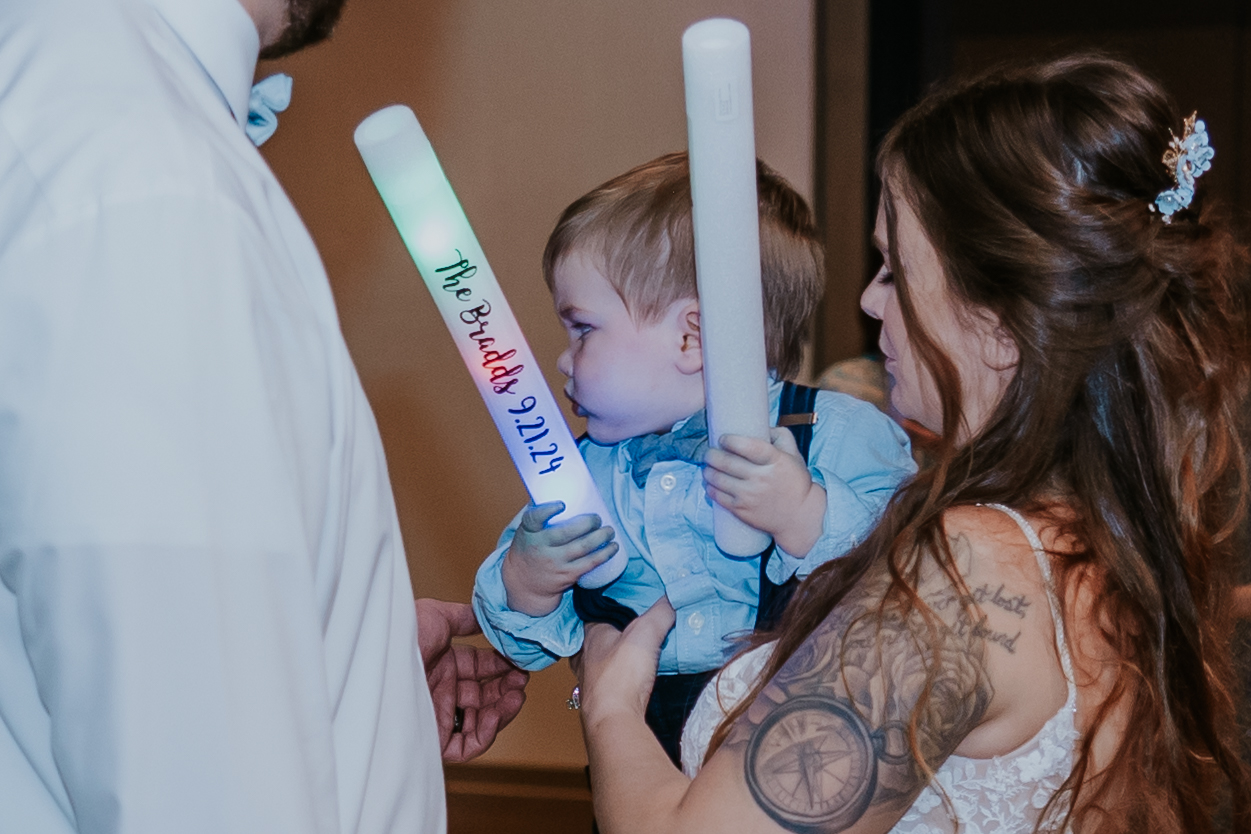 Bride holding a young child with customized LED foam sticks — a fun and thoughtful reception detail that adds to the list of unique wedding ideas.