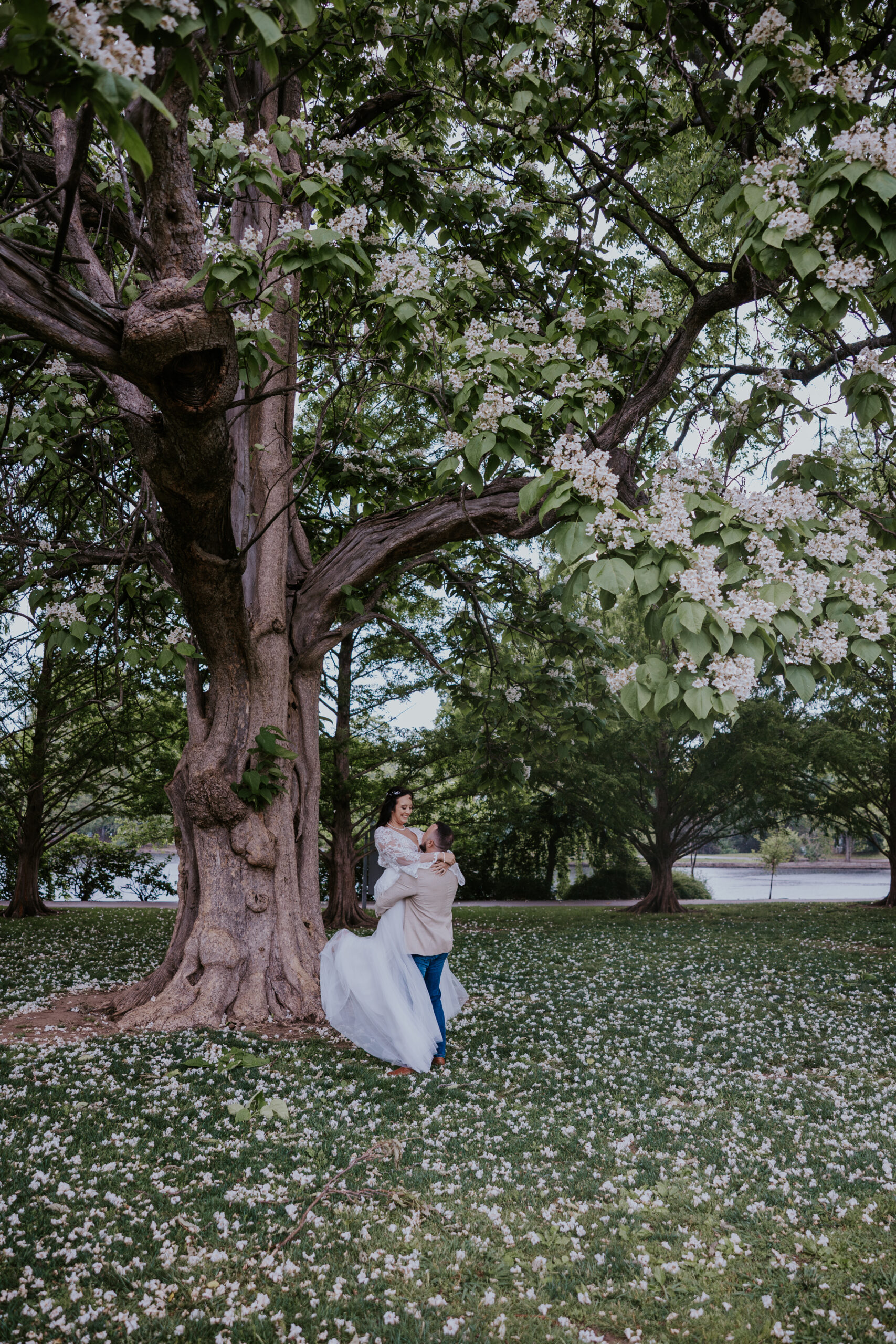 Joyful moment as groom lifts bride under a blooming tree—captured by a travel wedding photographer in a scenic outdoor location.