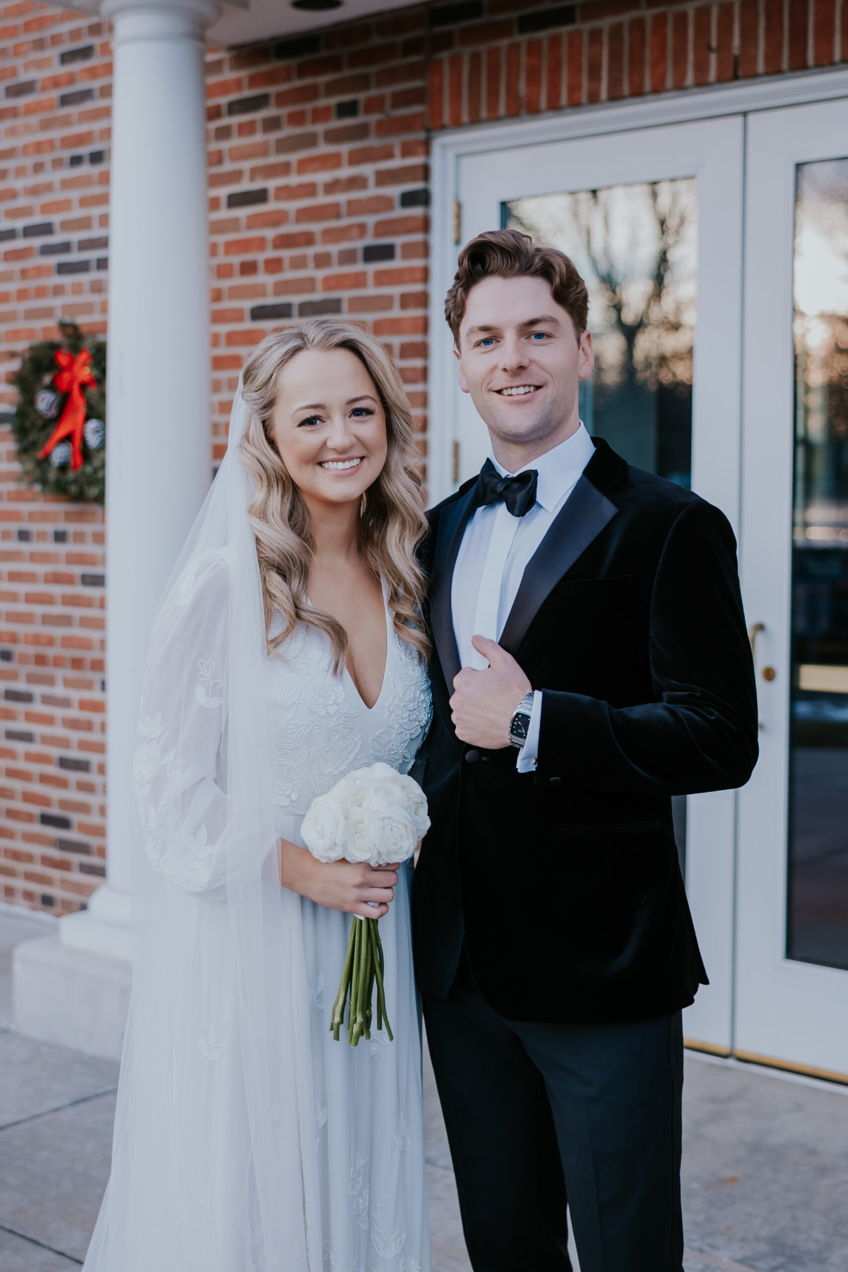 Bride holding a white bouquet while standing next to the groom outside a brick building, captured by a wedding photographer in Minnesota.
