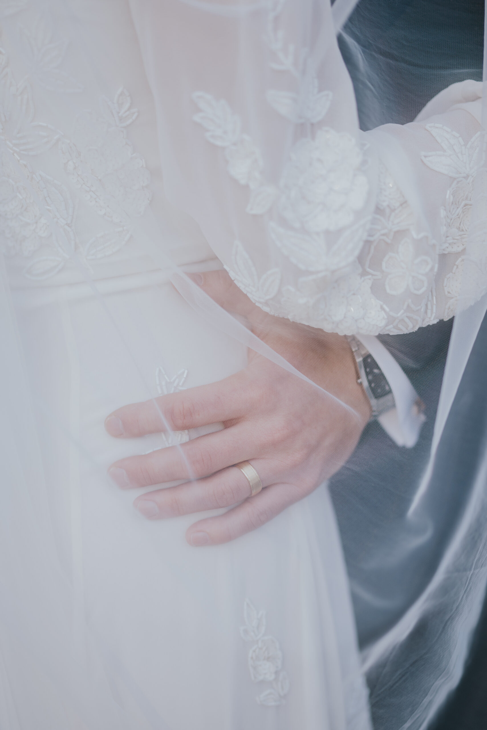 Close-up of the groom’s hand resting on the bride’s waist, showing a simple gold wedding band.