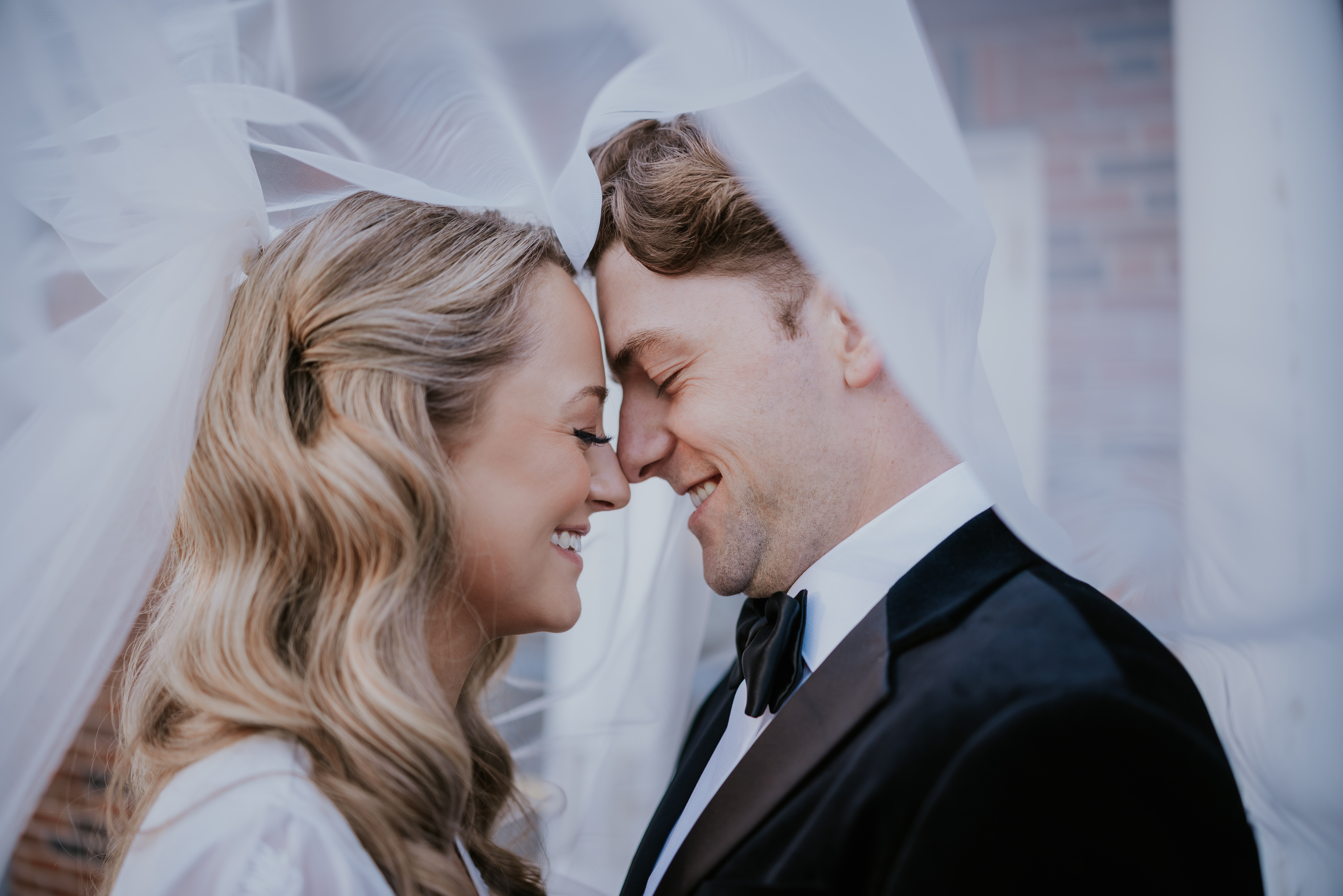 Bride and groom forehead to forehead under the bride’s veil, both smiling softly.