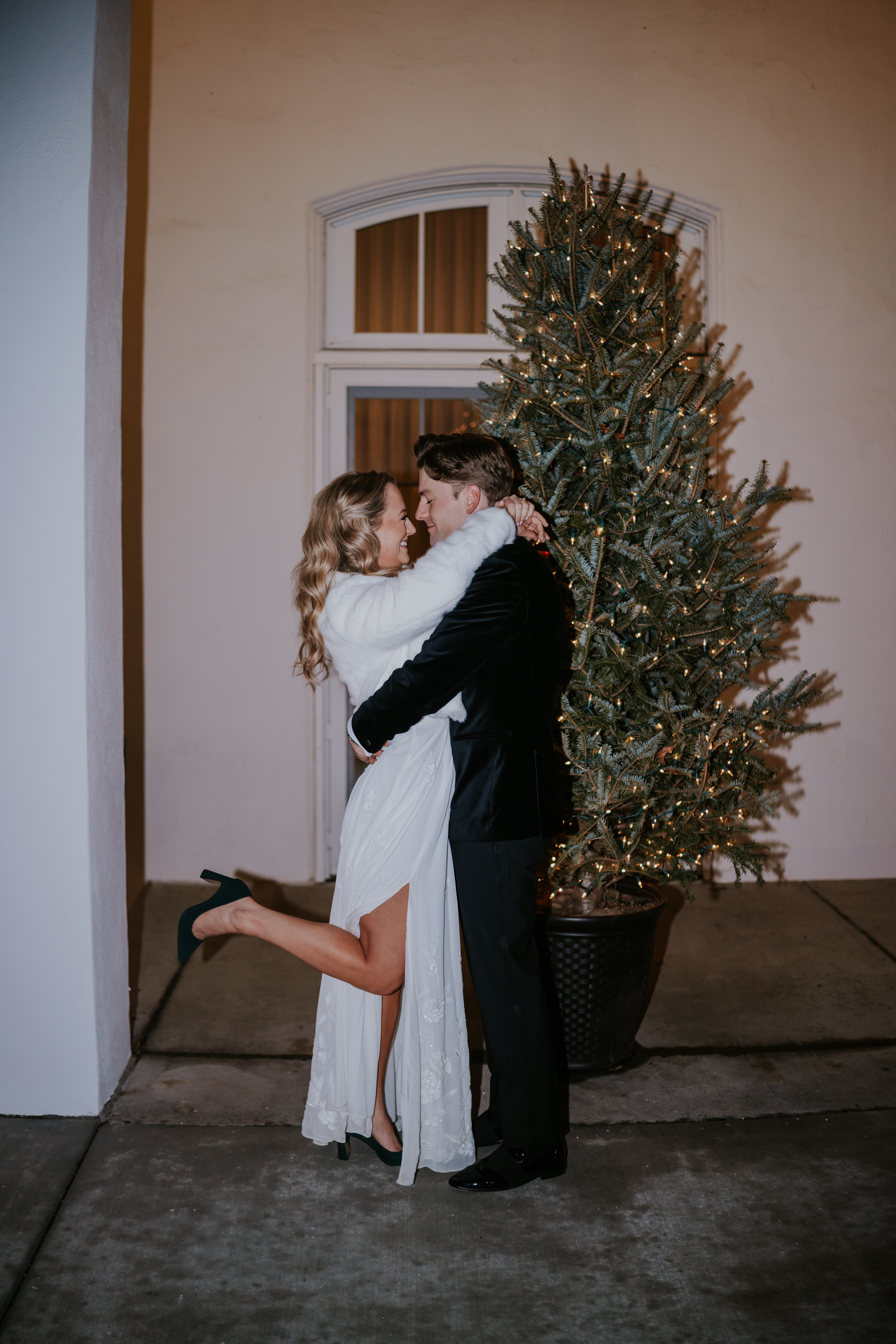 Bride and groom embracing outside at night next to a Christmas tree with twinkling lights, photographed by a wedding photographer in Minnesota.